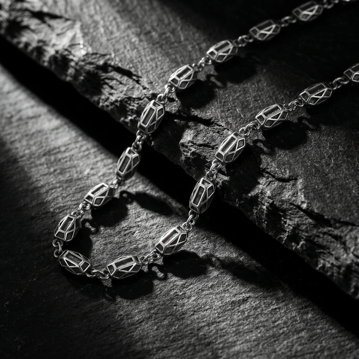 Close-up of the silver geometric link necklace lying on a dark textured slate background.