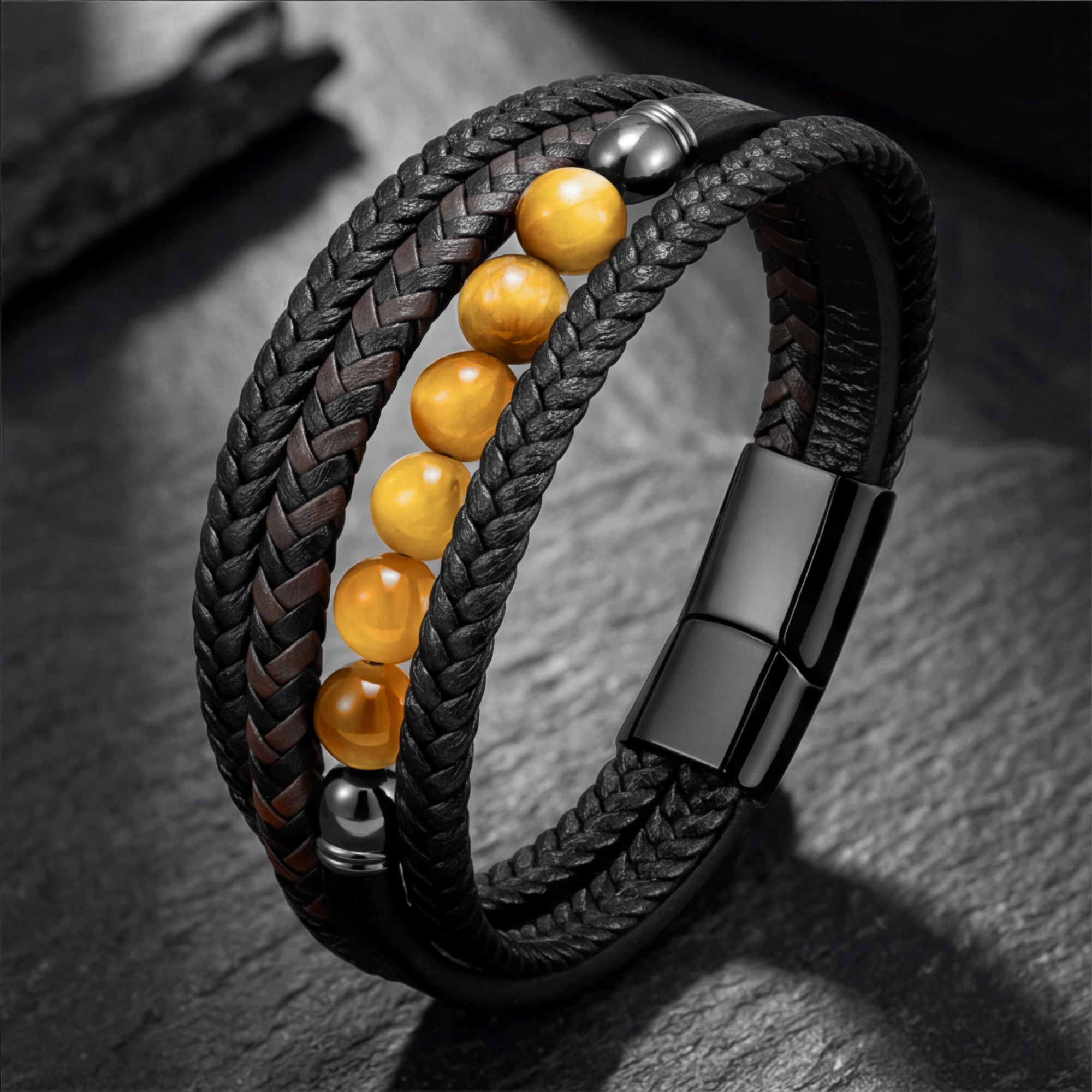 Black braided leather bracelet with round yellow tiger eye beads and black stainless steel clasp on a stone surface.