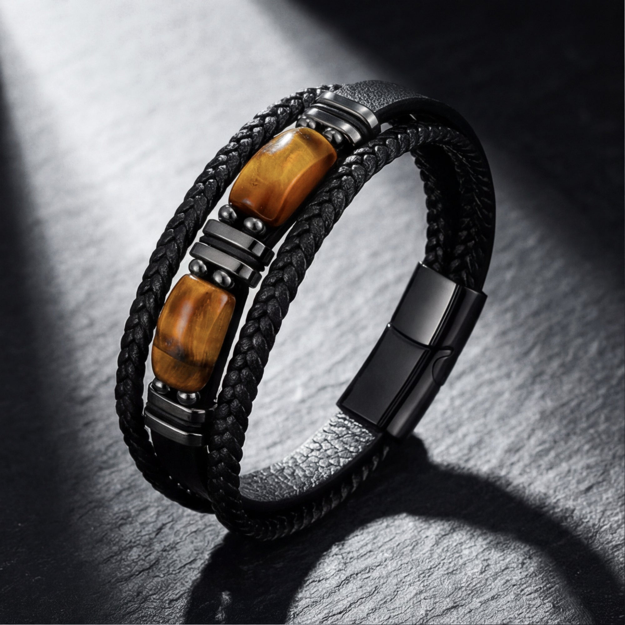 Black braided leather men's bracelet with natural Tiger's Eye stones and black stainless steel on a slate background.