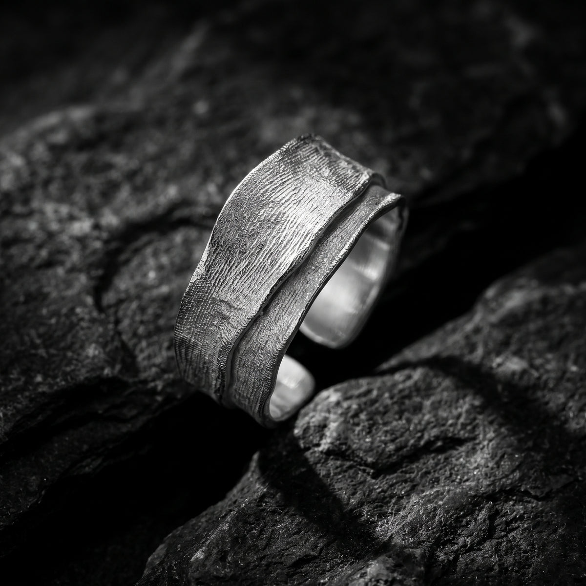Angled close-up of the textured silver overlap ring resting on dark rock