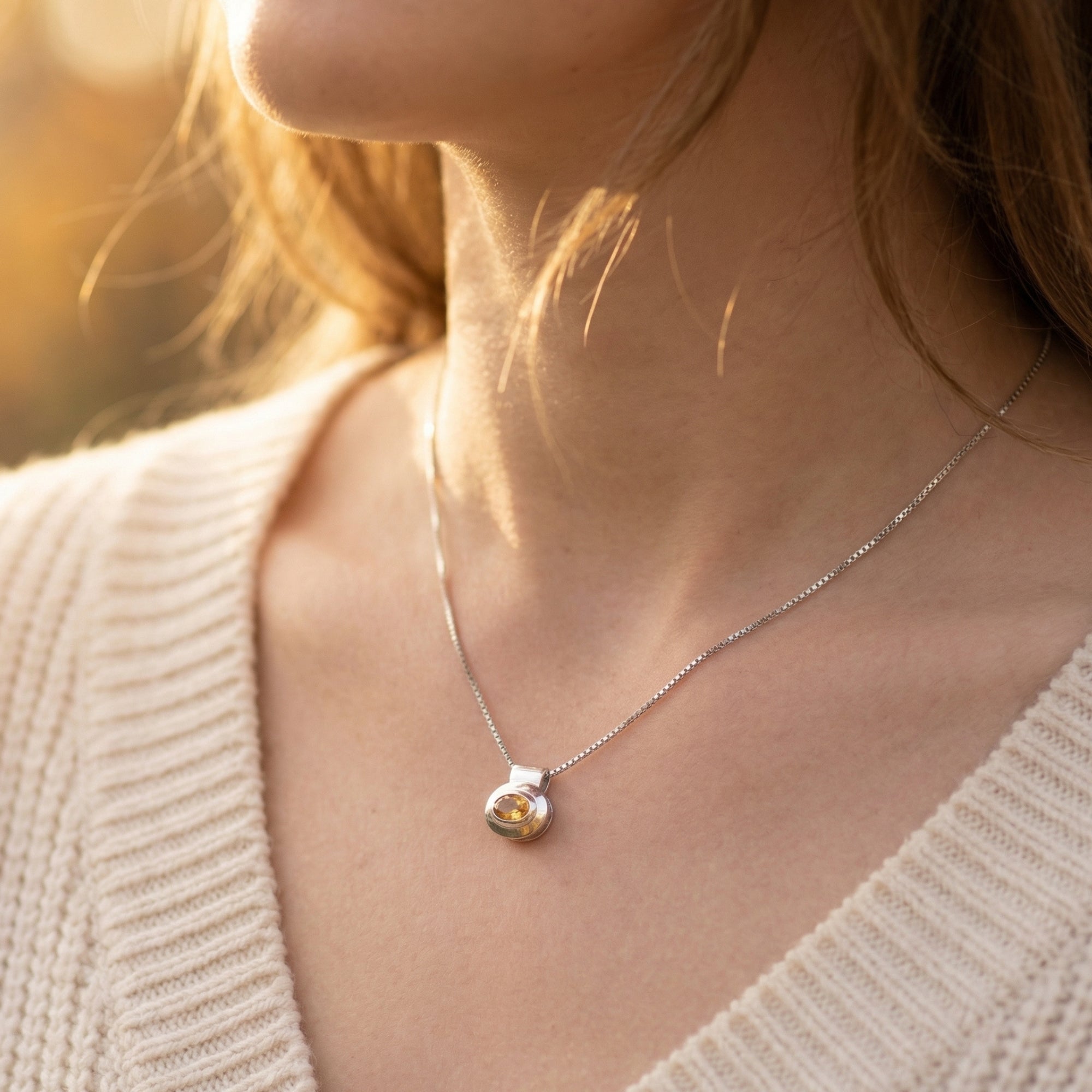 Side view of a woman wearing the Aelia natural citrine pendant necklace in silver over a cream sweater.