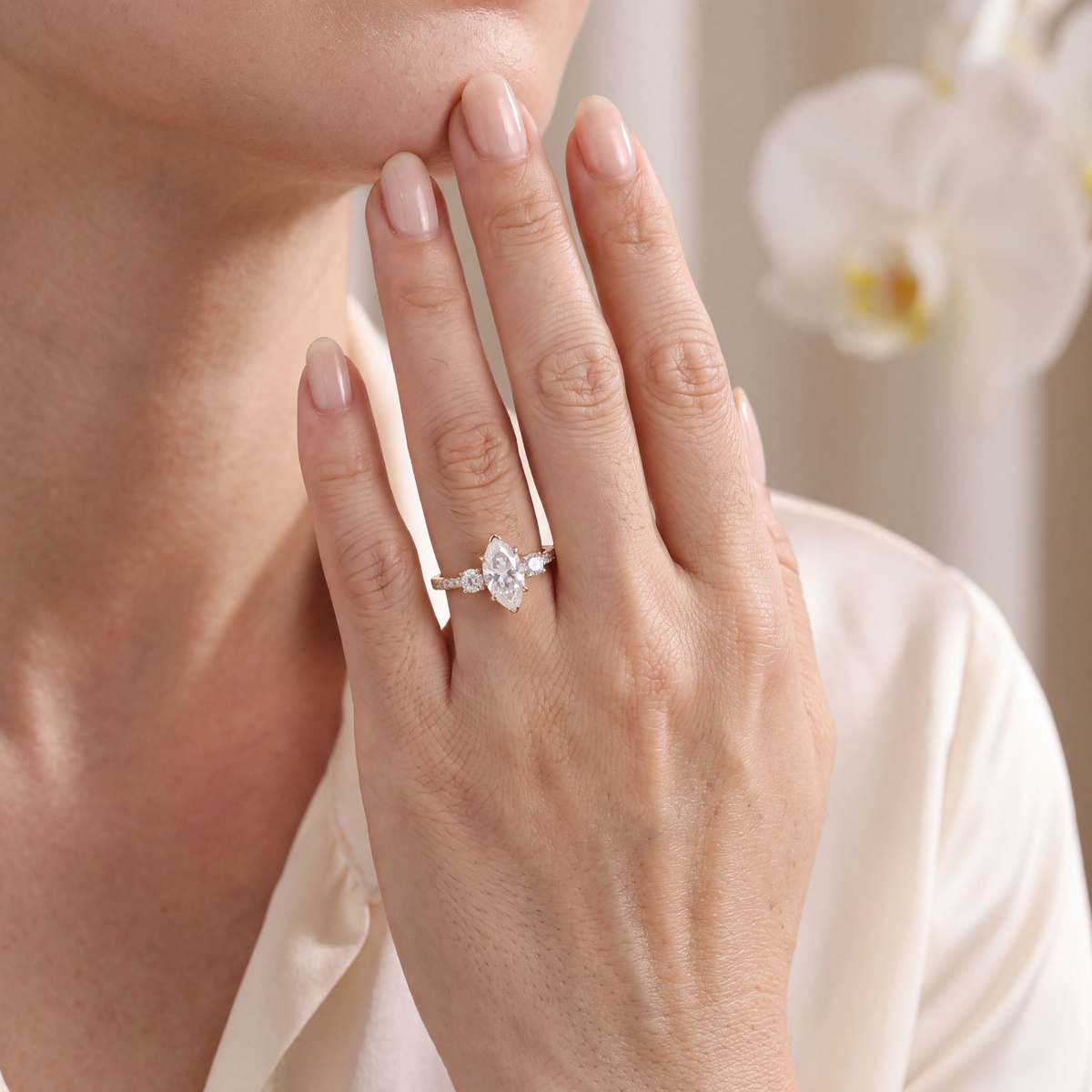 Close-up of a hand wearing a yellow gold marquise cut moissanite three-stone engagement ring.