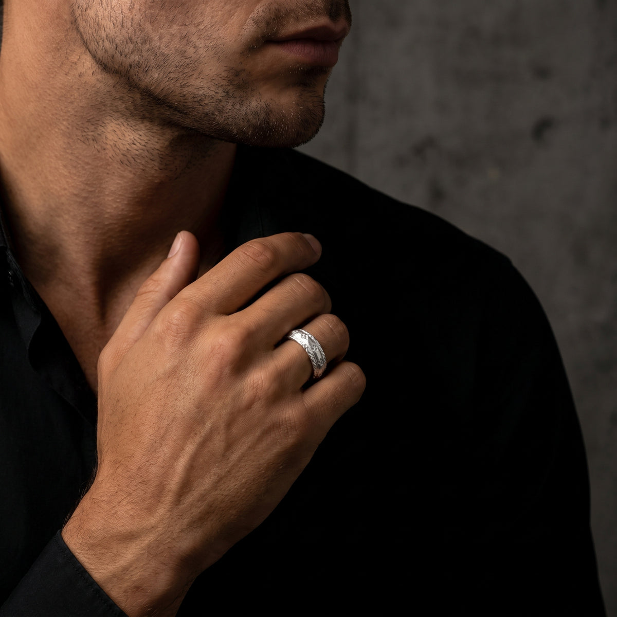Man in a black shirt wearing the etched silver open band ring on his finger, hand raised near his chest.