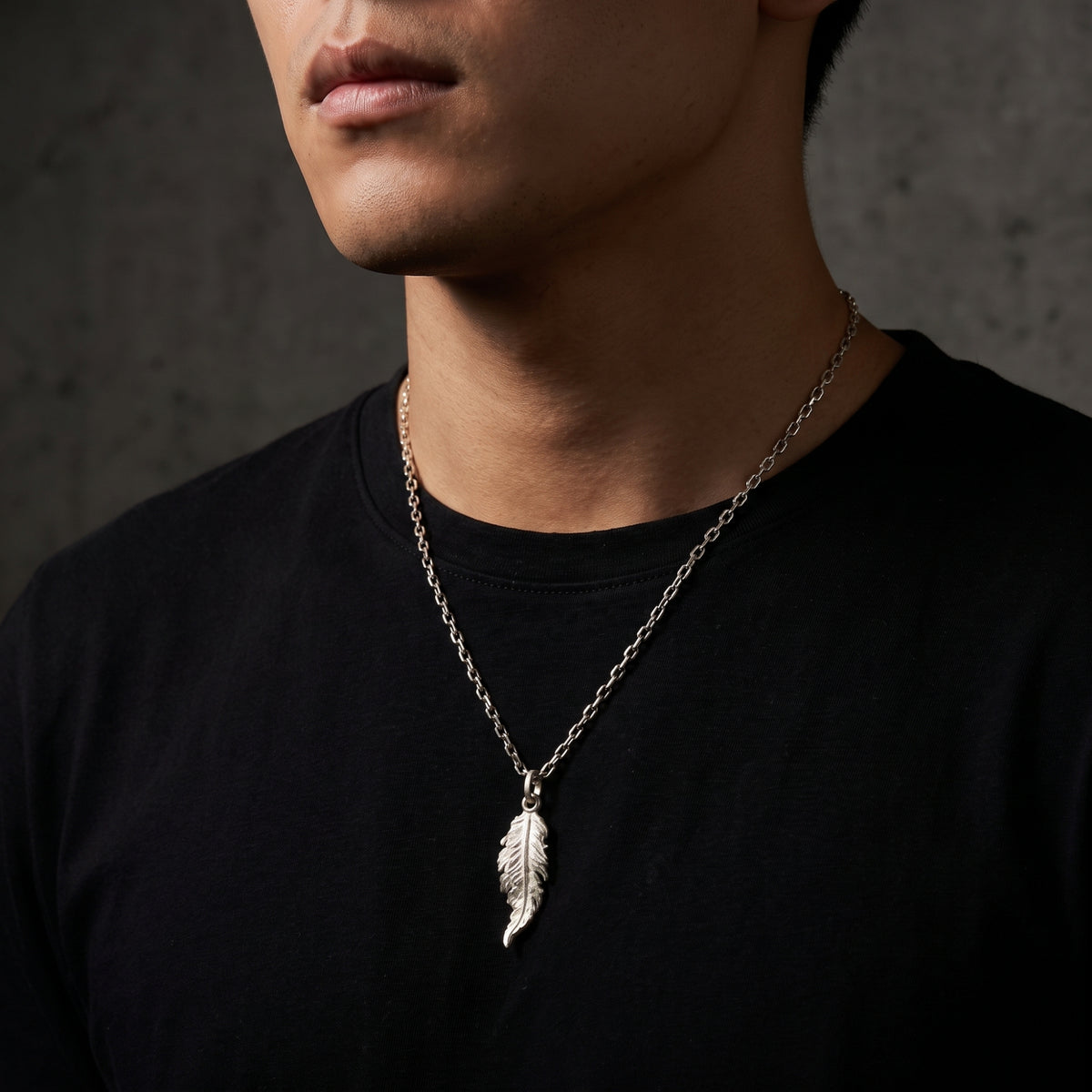 Man wearing the silver feather pendant necklace on a chain over a black T-shirt.