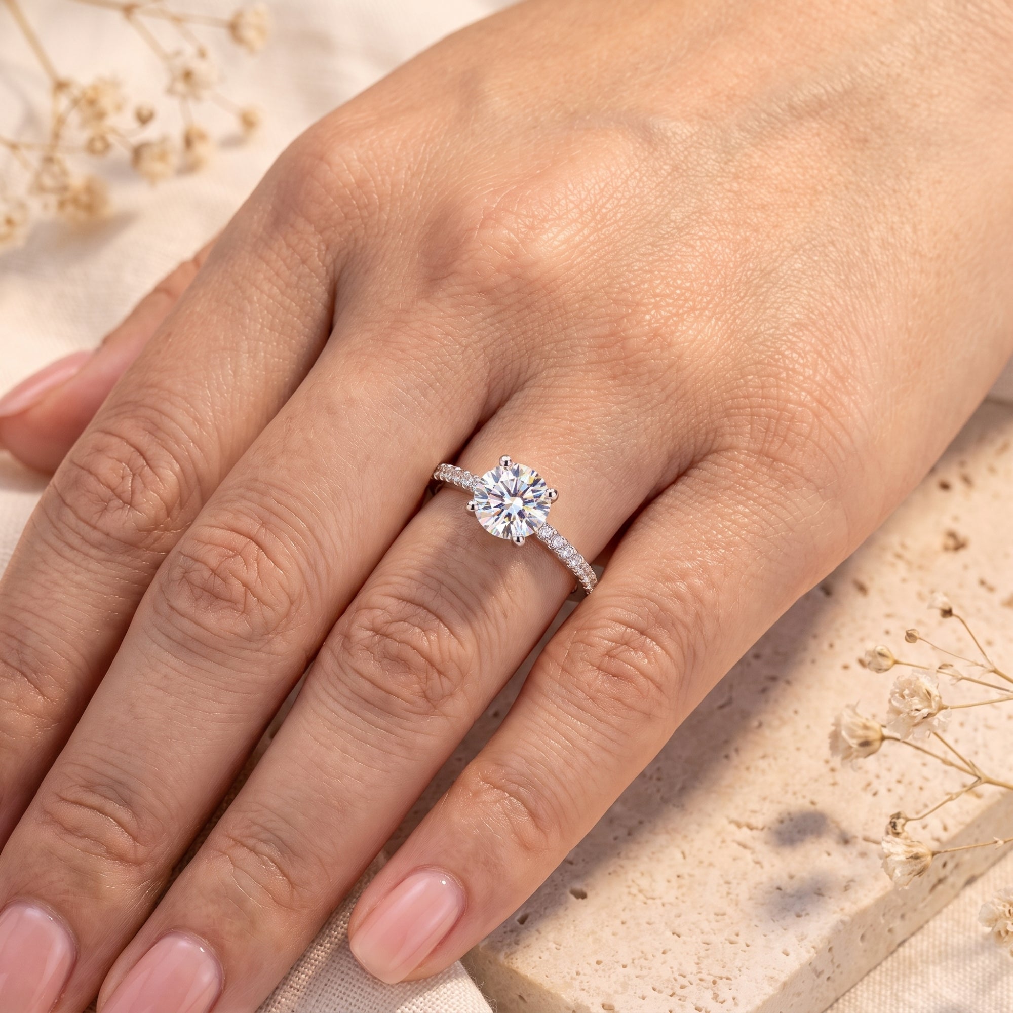 Top view of the silver ring with a round clear center stone worn on a hand against a light neutral background.