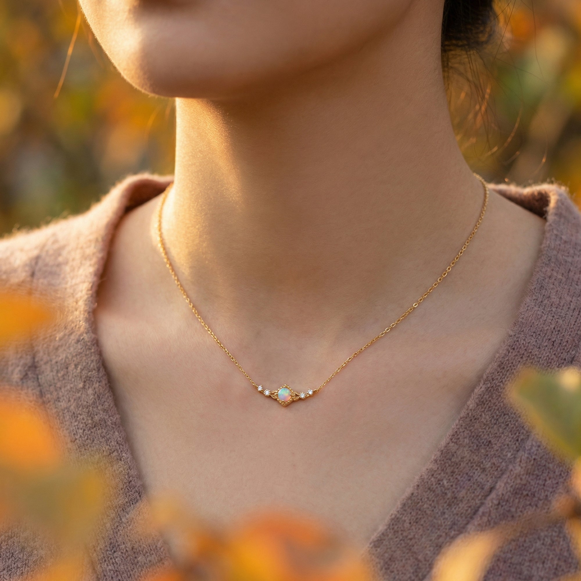 Model wearing the gold-tone Callisto Column necklace with a round white opal pendant against an autumn background.