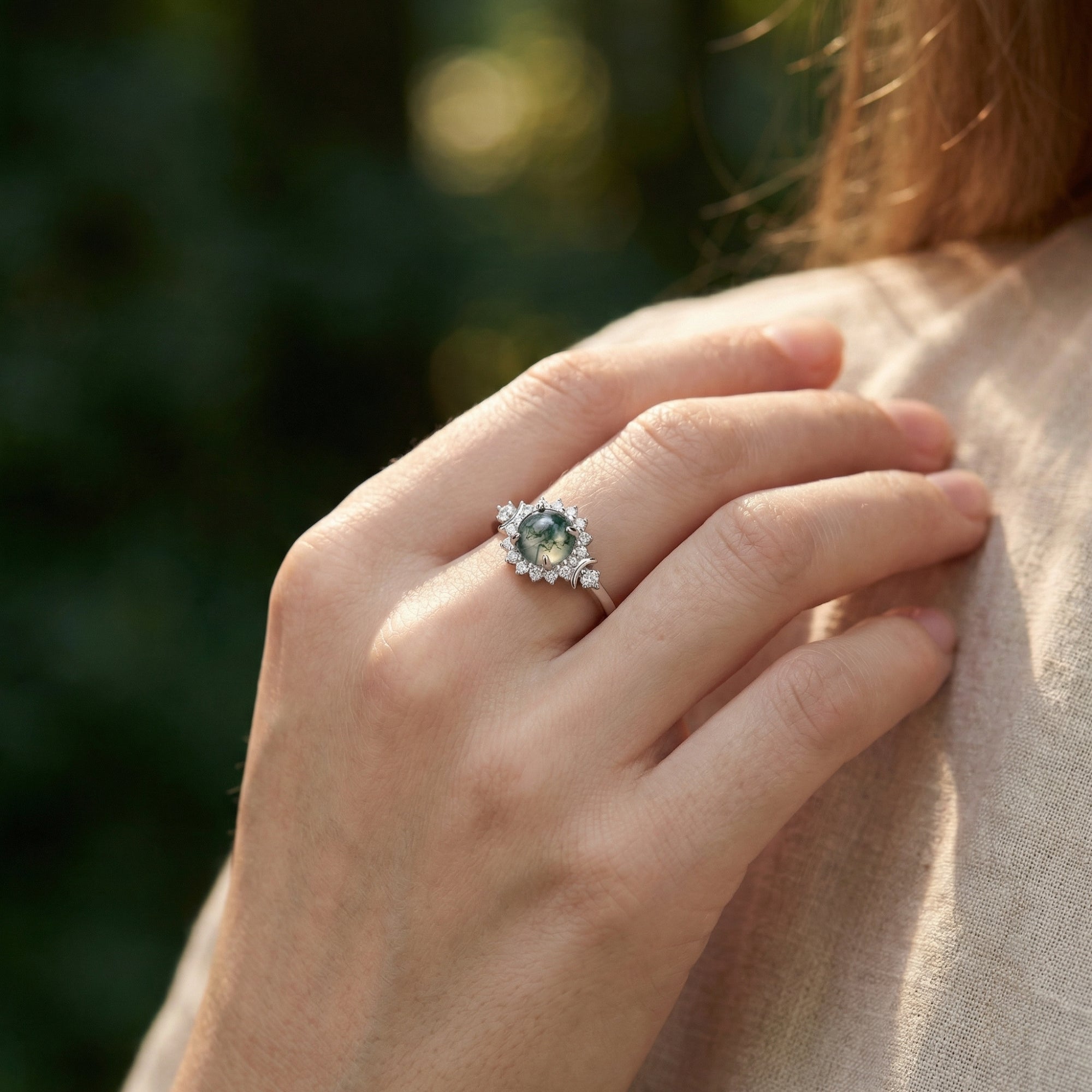Sterling silver floral halo ring with a round moss agate stone worn on a woman's hand in natural light.