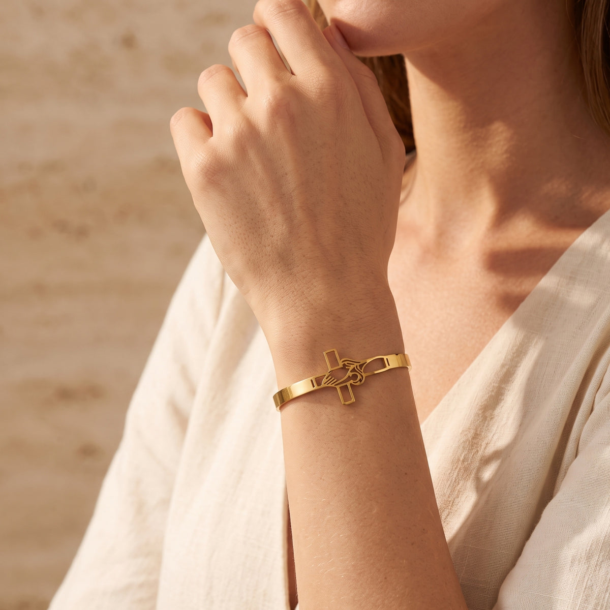 Close-up of a model wearing the gold-tone praying hands and cross cuff bracelet on her wrist.