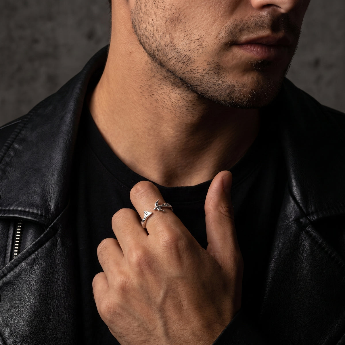 Man in a black leather jacket wearing the open-band mountain and bird ring on his index finger.
