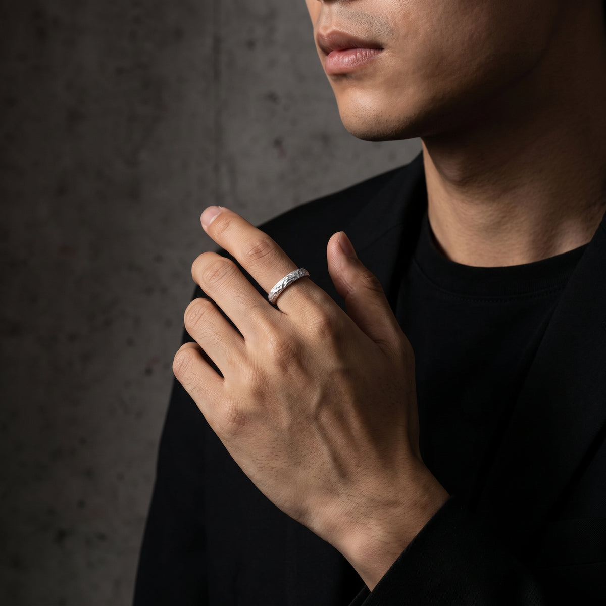 Model wearing the textured silver ring on his ring finger, with his hand held near his chest against a gray wall.