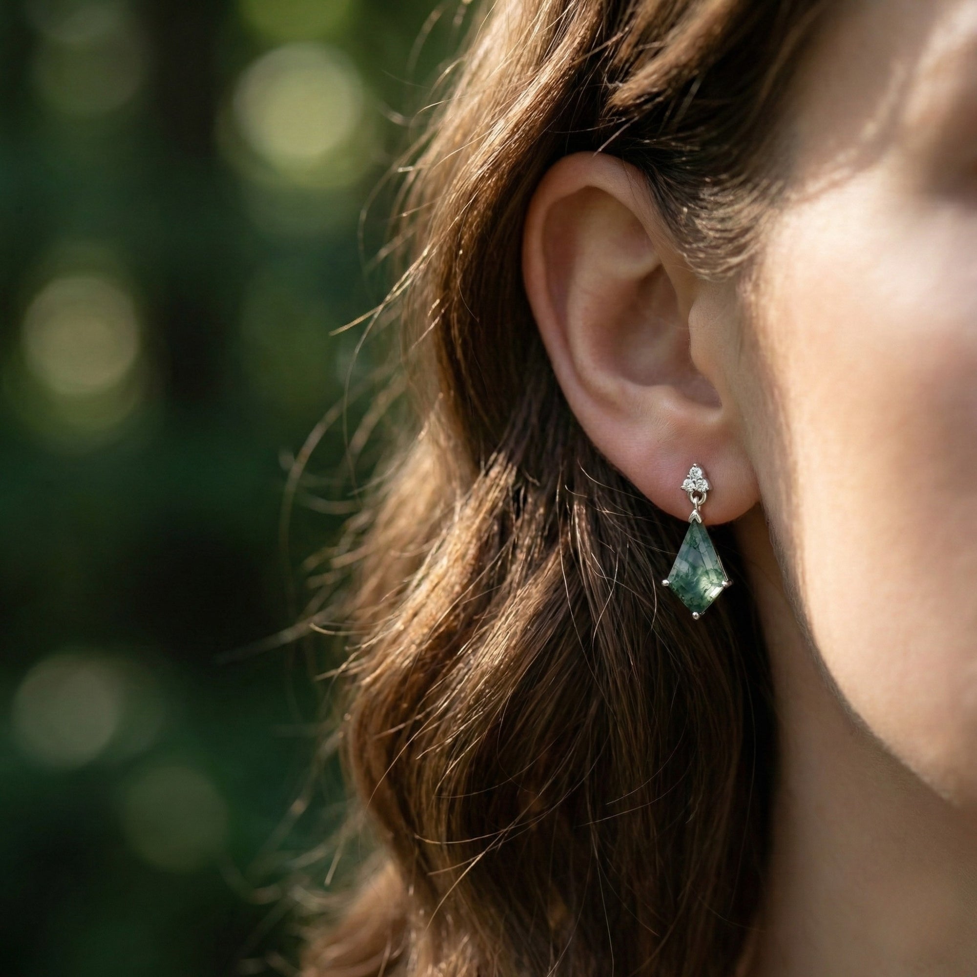 Side profile of a model wearing a kite cut moss agate drop earring in sterling silver.