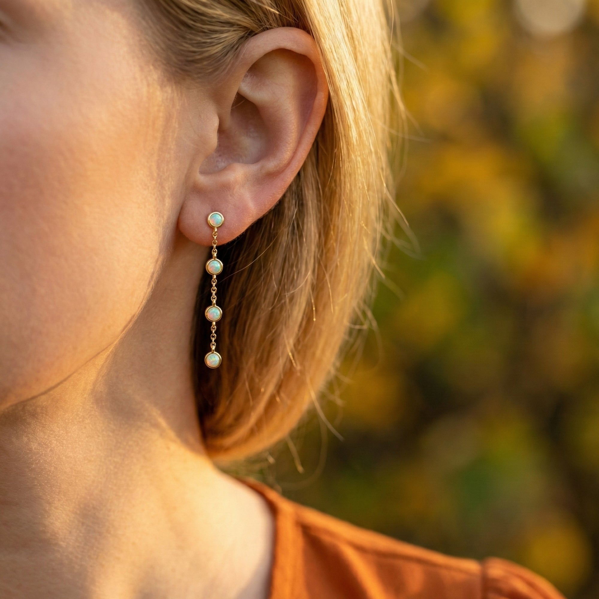 Arianell gold drop earring with four natural white opals worn on a woman's ear in soft outdoor light.