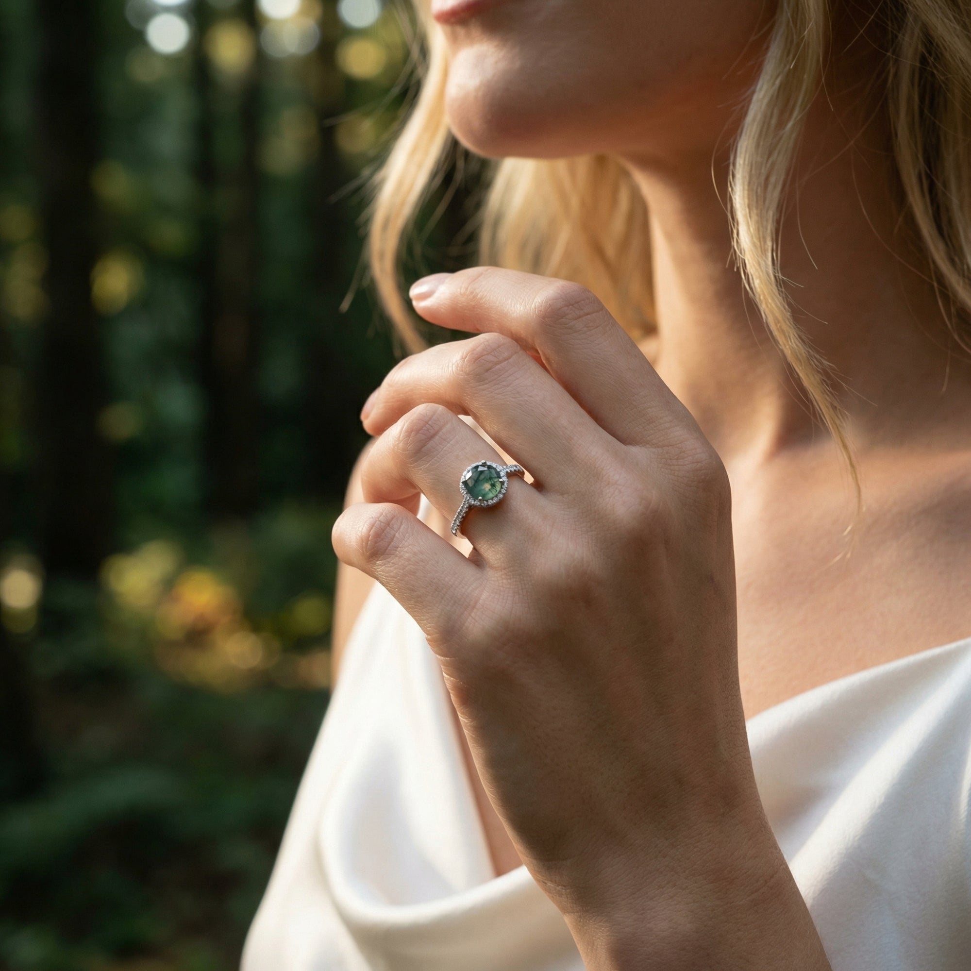 Woman wearing the oval moss agate and diamond halo ring in sterling silver, styled in a natural forest setting.