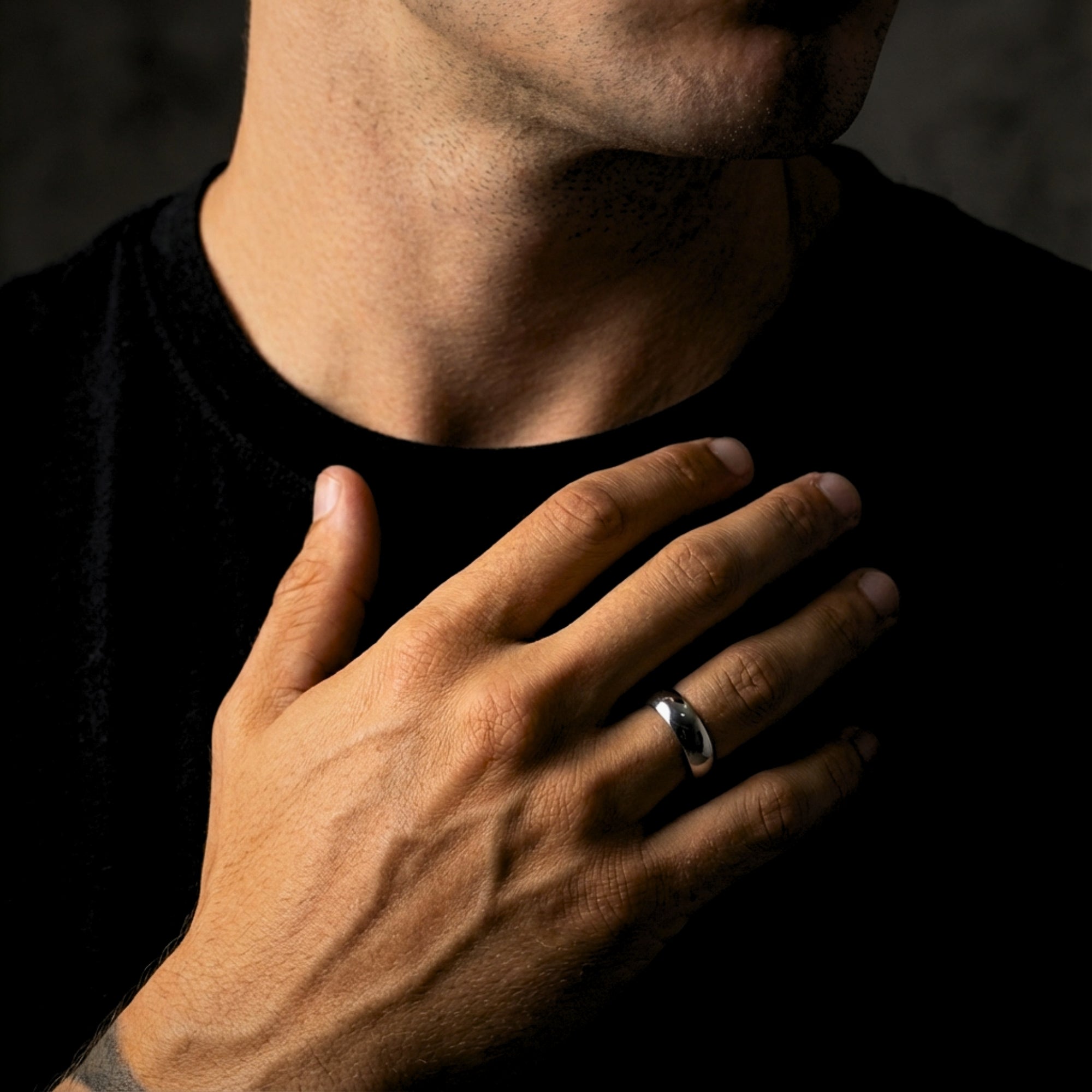 The Minimalist Ring, a silver 5mm stainless steel band for men, worn on a hand over a black shirt.