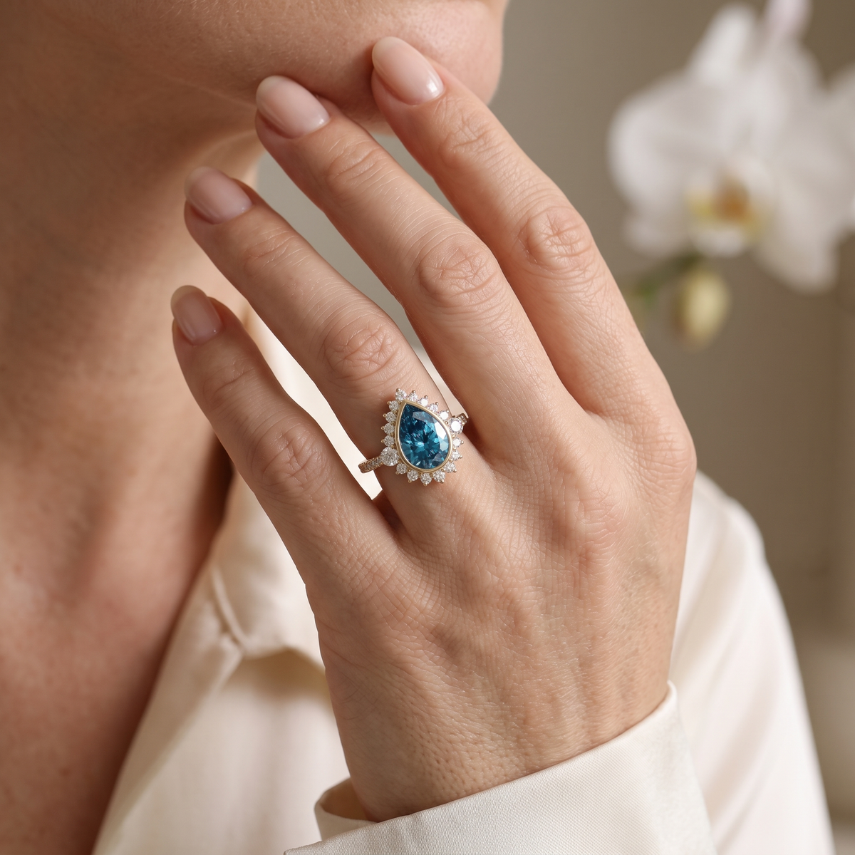 Woman wearing a pear cut blue moissanite halo engagement ring in rose gold.