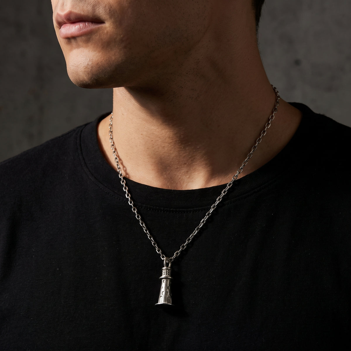 Close-up front view of a model wearing the silver lighthouse pendant necklace over a black T-shirt.