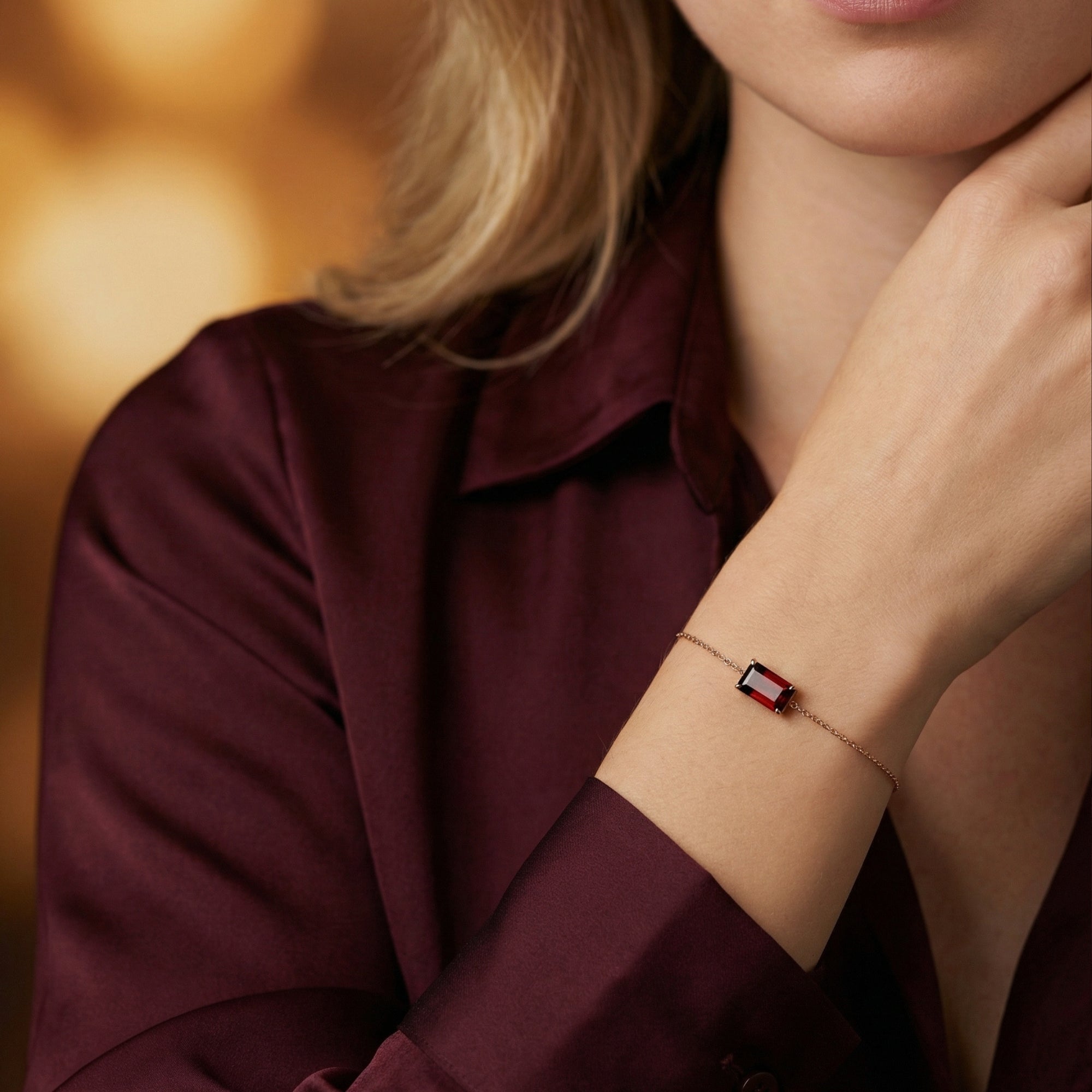 The Rosalind emerald-cut garnet bracelet in 18K rose gold worn on a woman's wrist with a burgundy silk blouse.