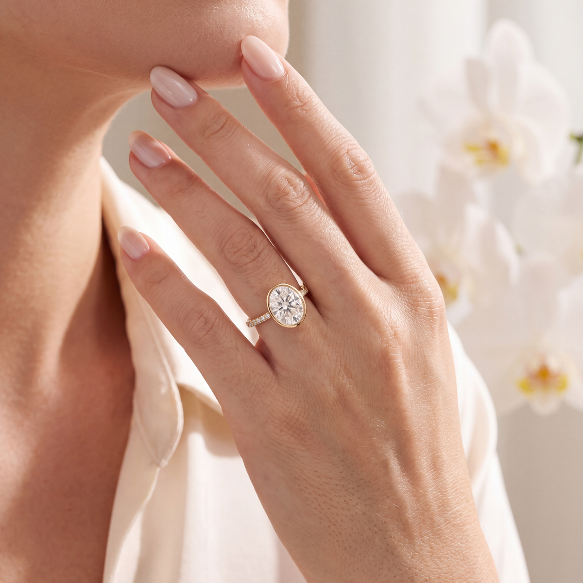 Model wearing a gold bezel-set oval moissanite ring with a pavé band.