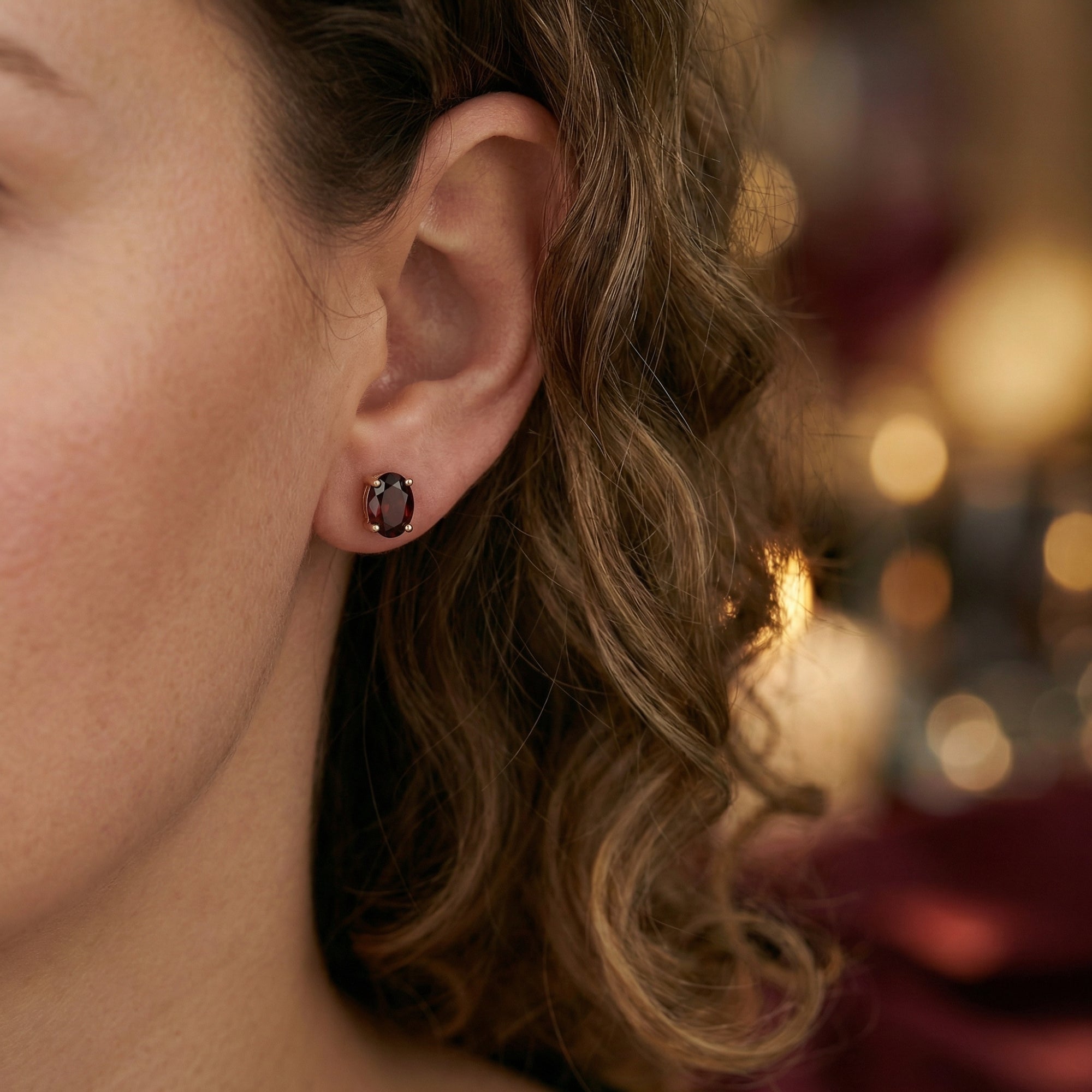 Woman wearing a Carina oval garnet stud earring in 18K rose gold on her ear.