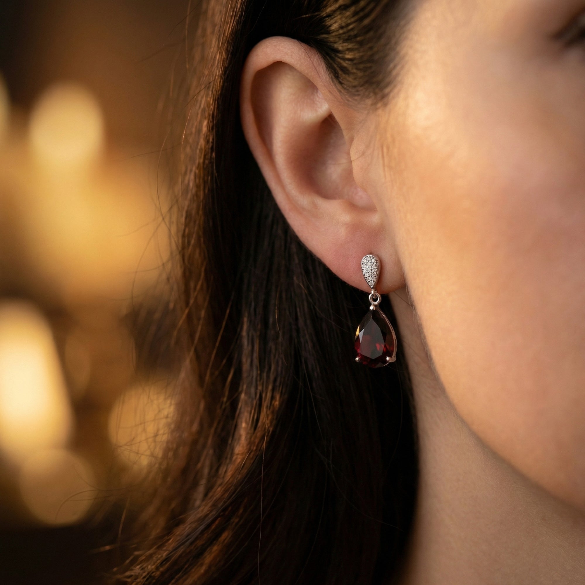 Woman wearing a sterling silver drop earring featuring a deep red pear cut garnet and shimmering accent stones.