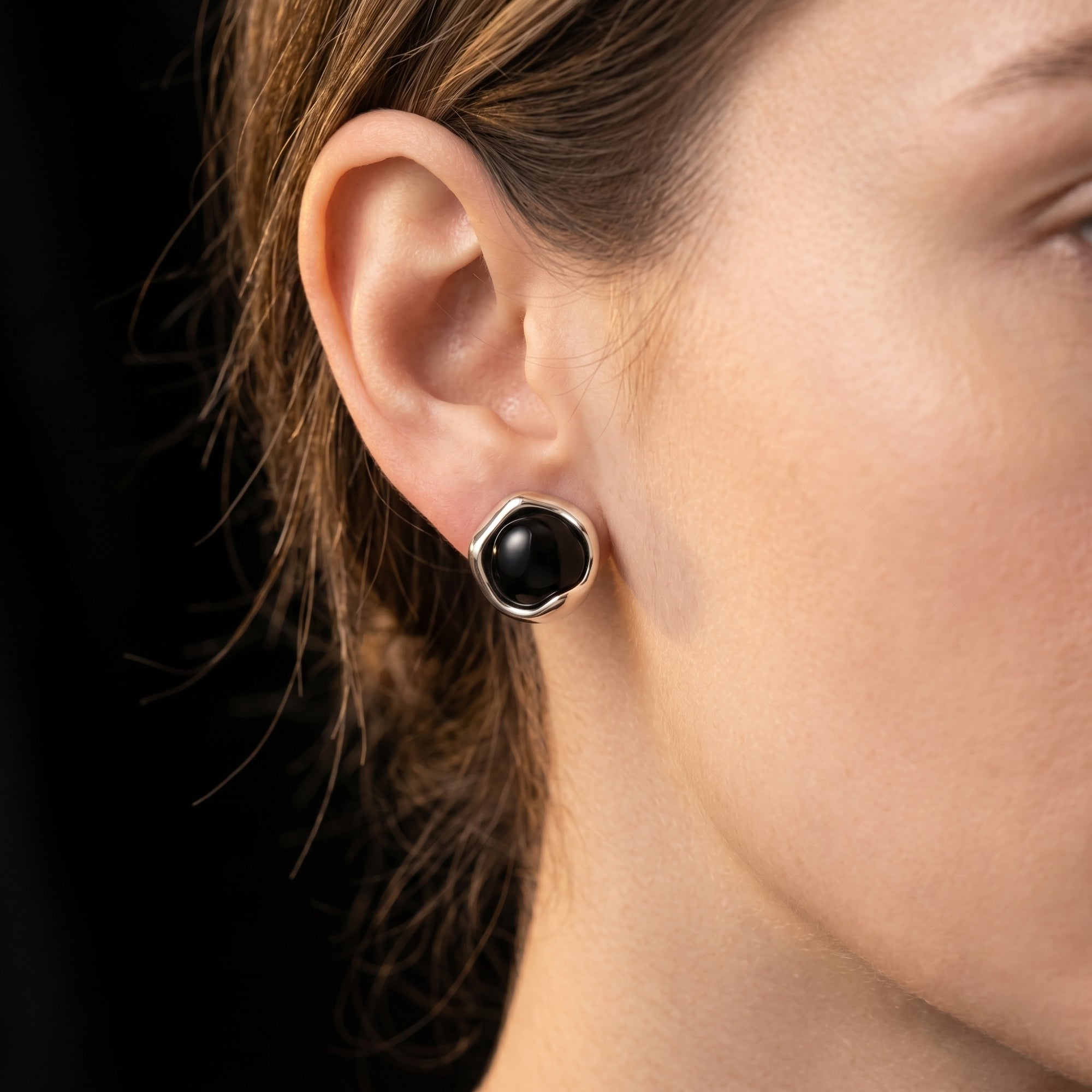 Close-up of a woman wearing a round black onyx earring in a silver architectural setting.