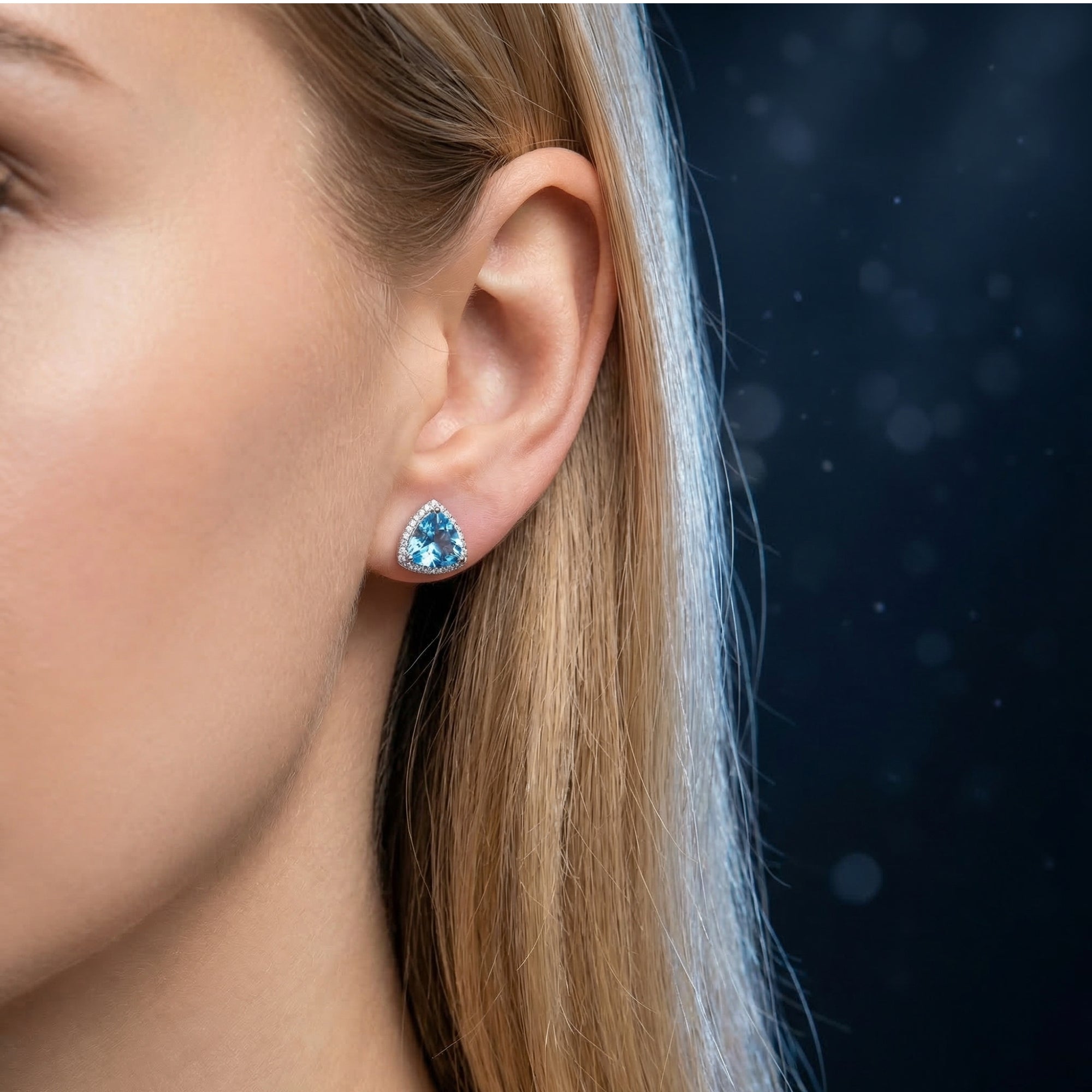 Woman wearing a silver triangle cut blue topaz earring with a halo setting on her ear.