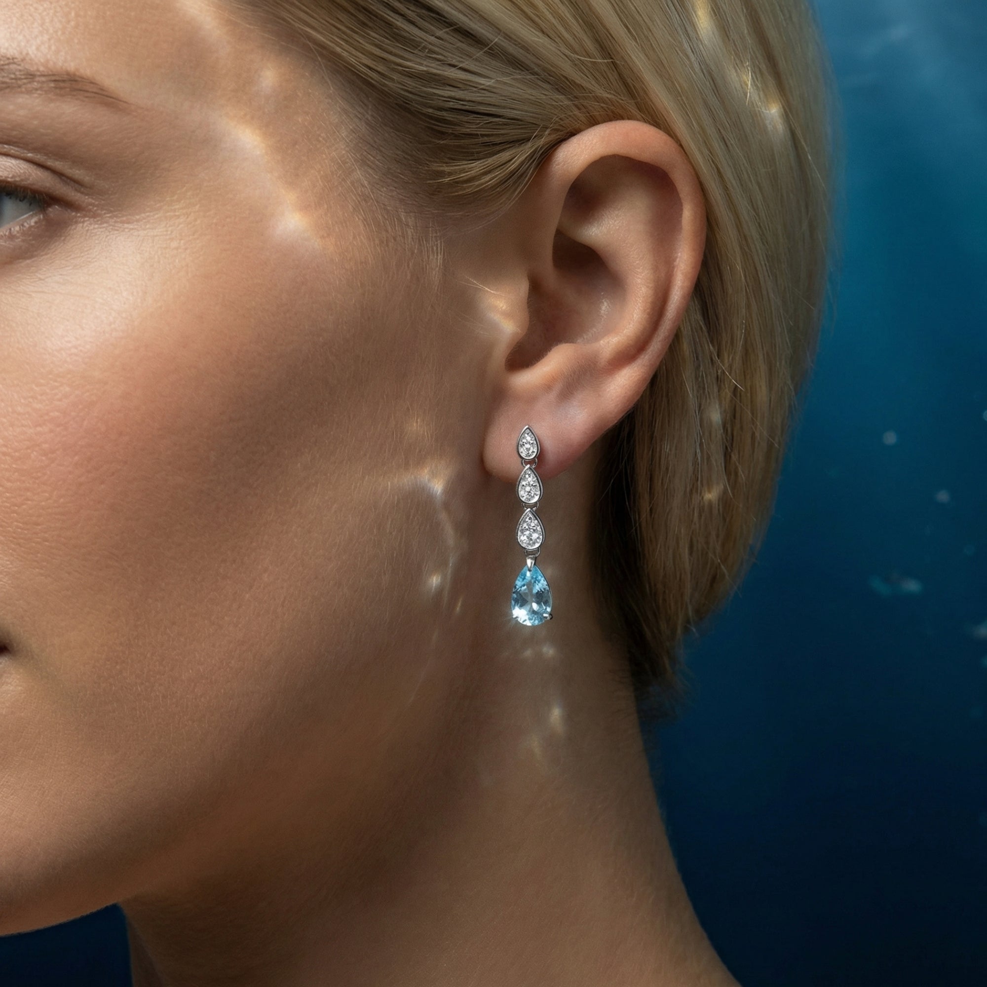 Woman wearing a platinum pear cut aquamarine drop earring against a blue background.