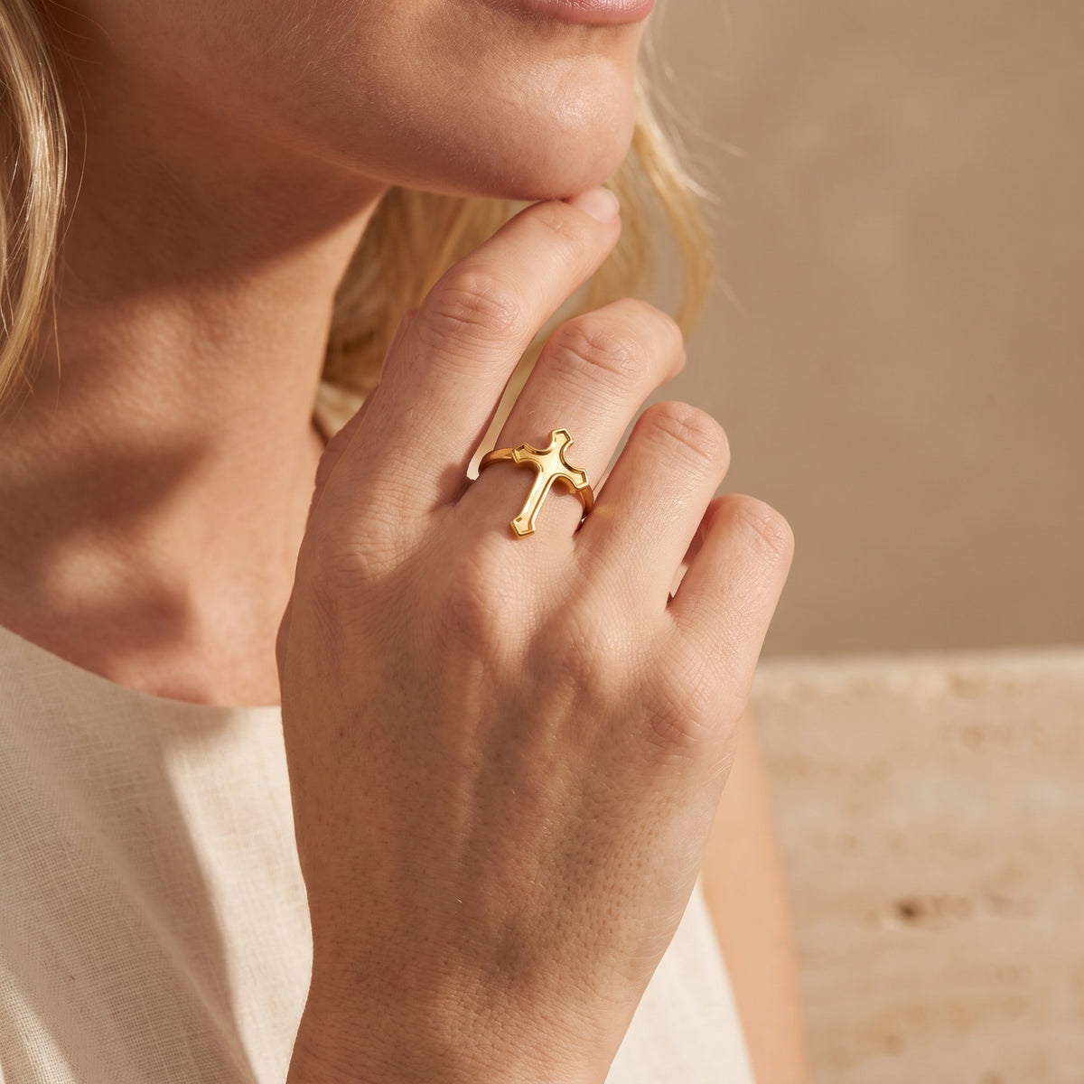 Close-up of a model wearing the gold-tone cross ring on her hand near her chin.