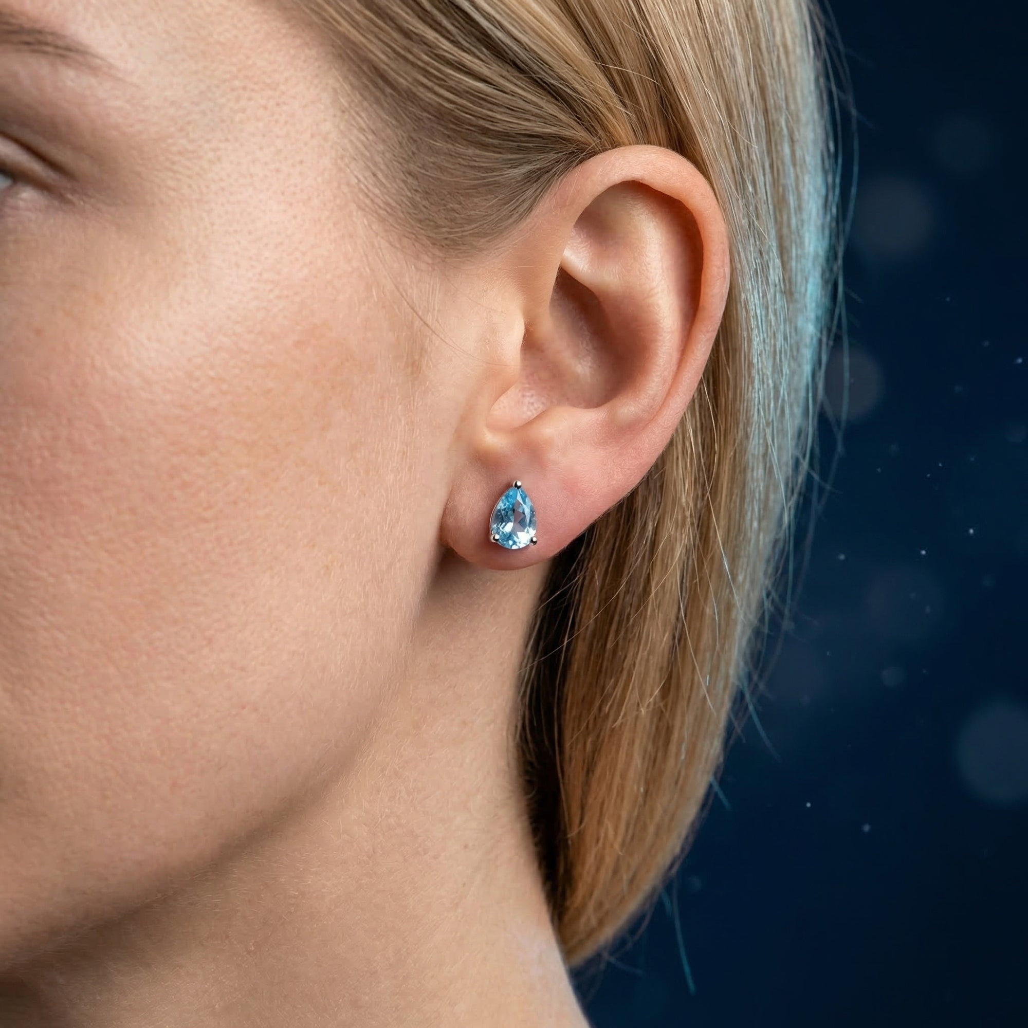 Model wearing a pear-cut Swiss blue topaz stud earring in white gold, showing the scale and color on the ear.