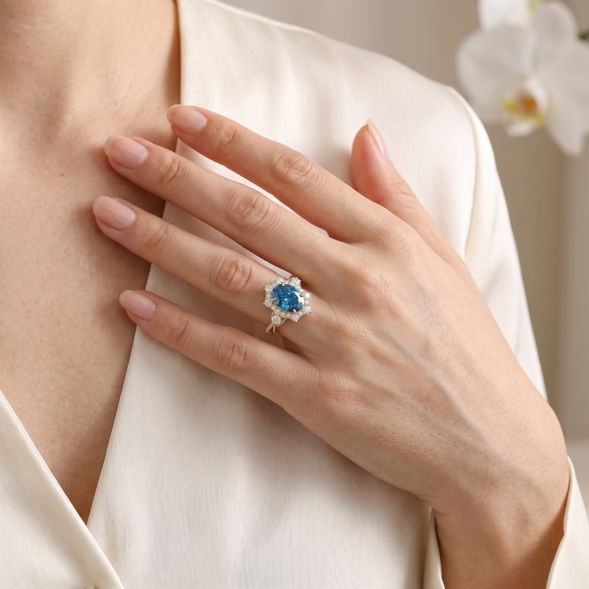 Woman wearing an oval blue moissanite halo engagement ring in rose gold against silk attire.