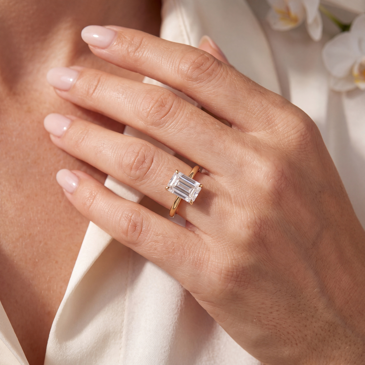 A hand wearing a yellow gold emerald-cut moissanite solitaire ring.