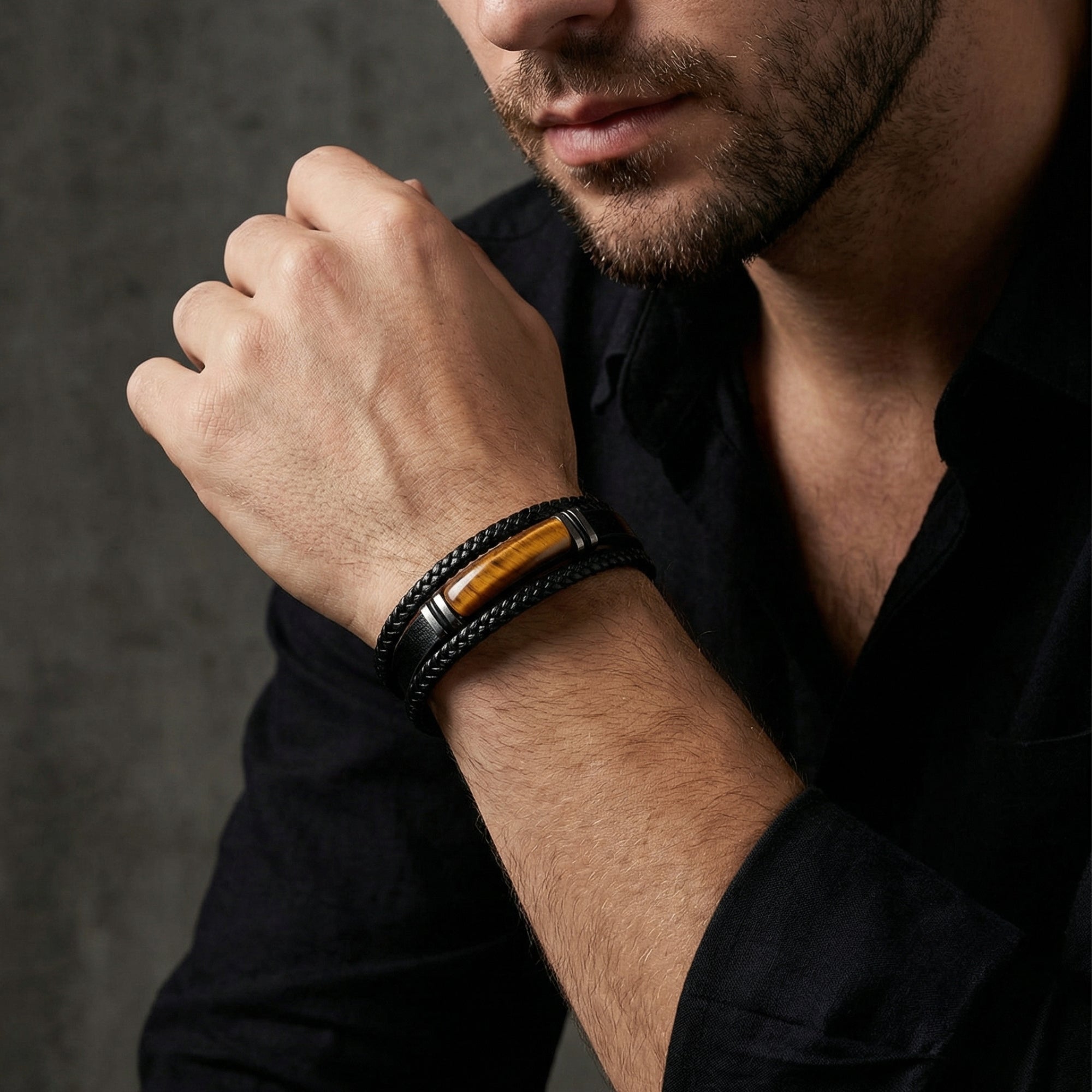 Men's black braided leather bracelet with tiger's eye stone and black steel accents worn on a model's wrist.