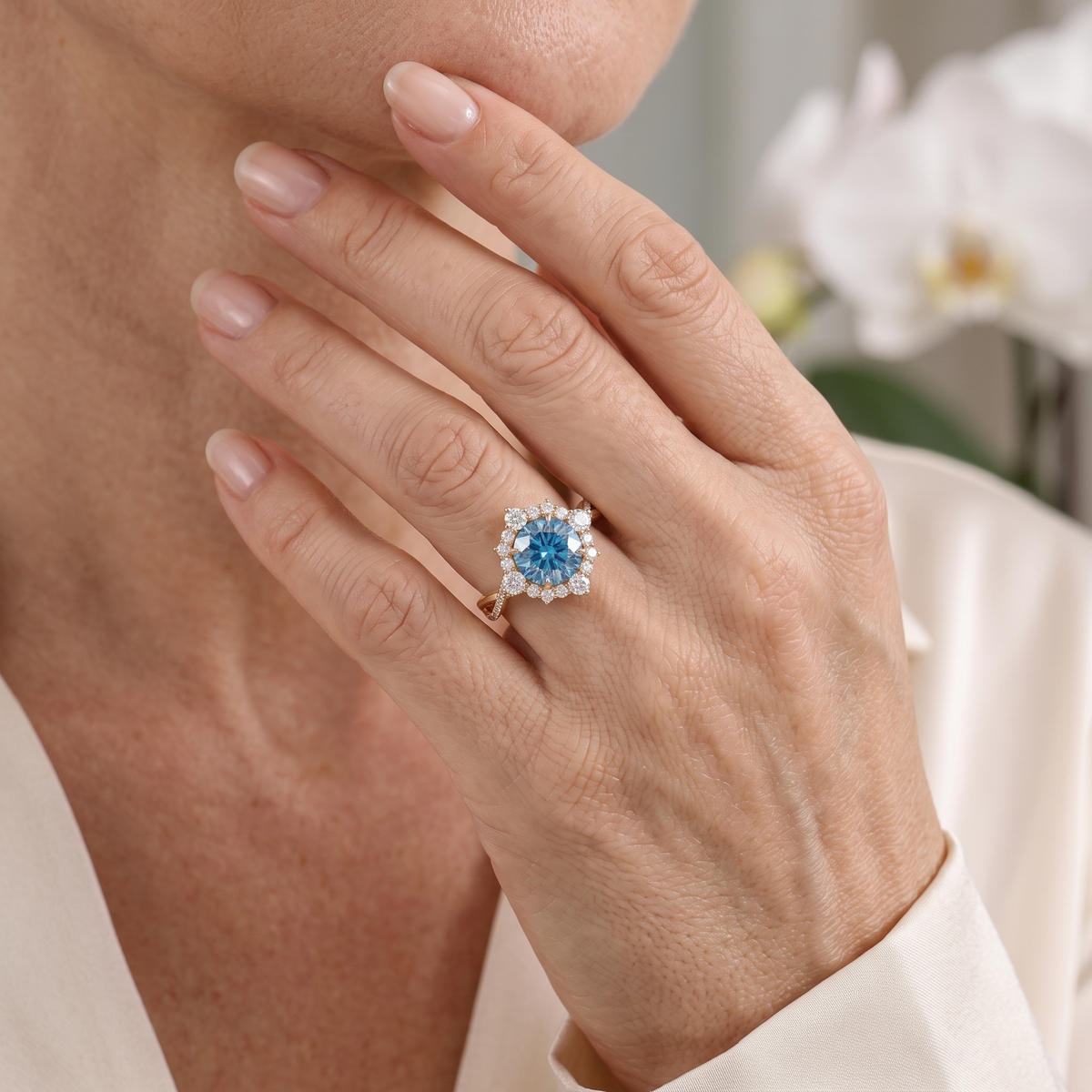 Close-up of a rose gold vintage halo ring with a blue moissanite center stone worn on a model's hand.