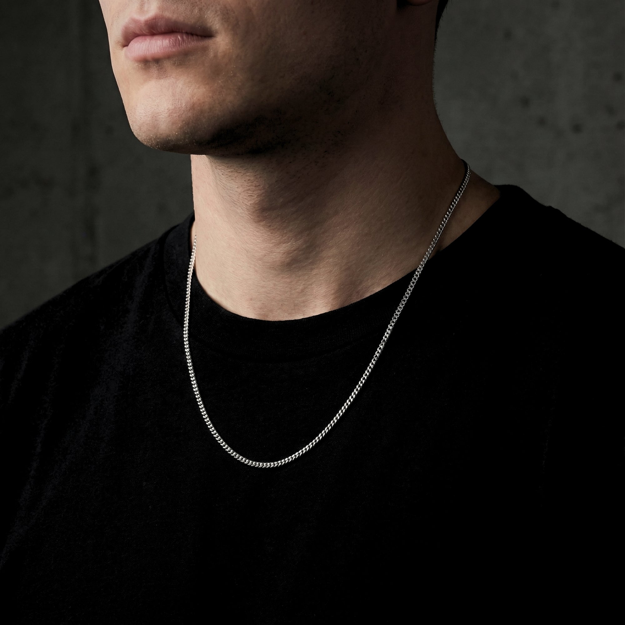 Men's 2mm silver stainless steel curb chain worn by a model over a black t-shirt.