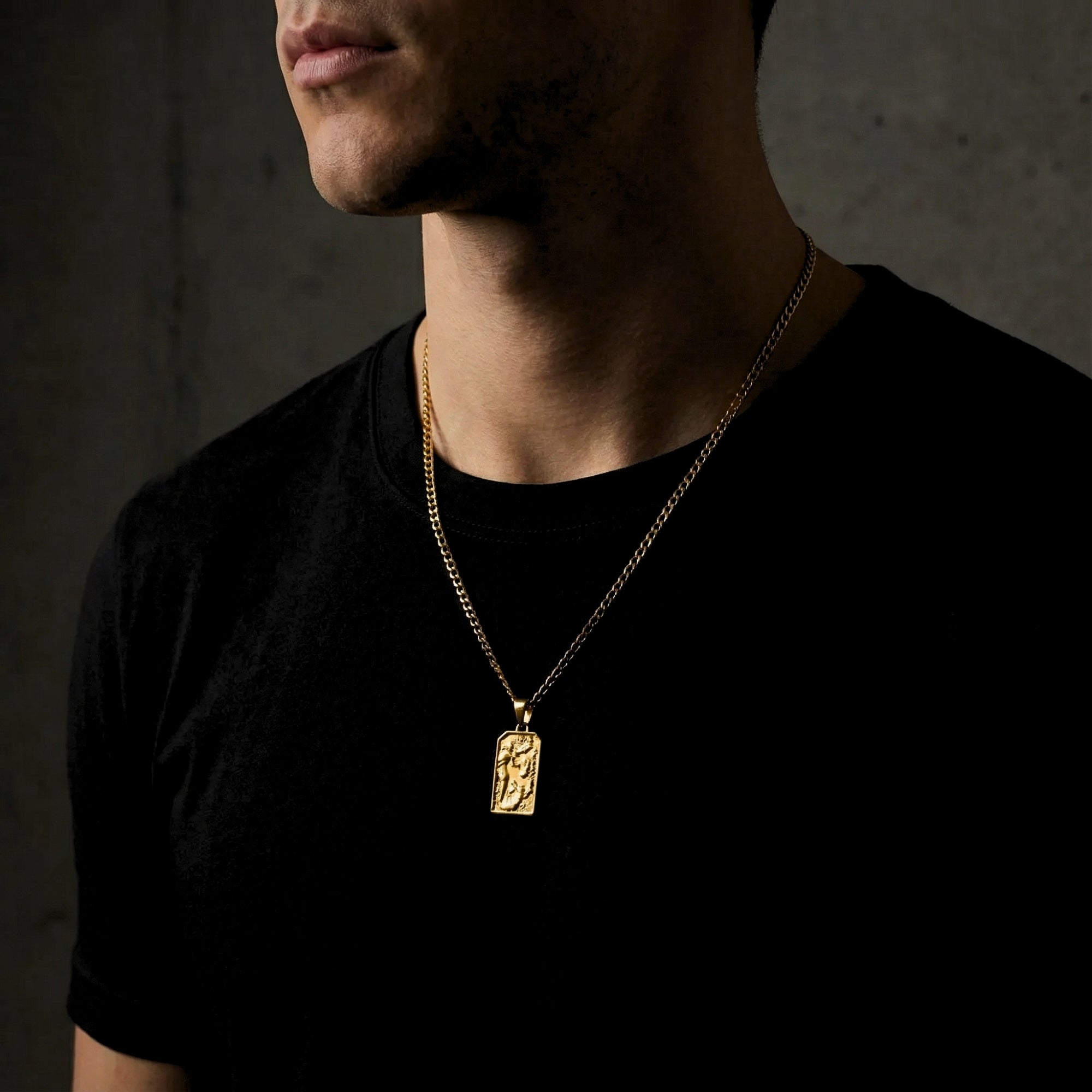 Male model wearing the gold stainless steel St. Michael Archangel pendant on a curb chain over a black t-shirt.