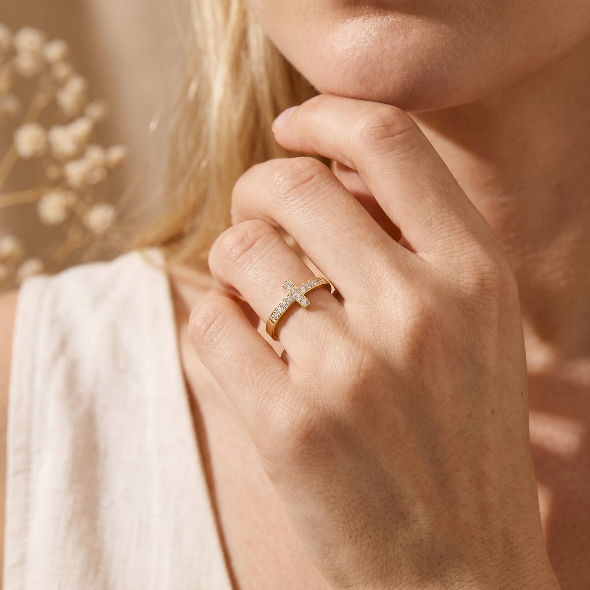 Close-up of a person wearing the gold-tone crystal cross ring with a hand raised near the chin.