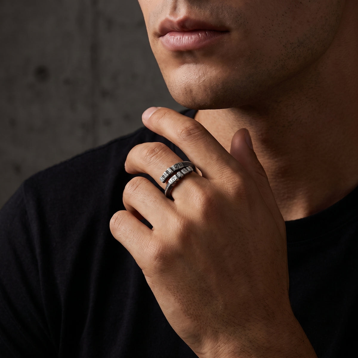 Close-up of a carved silver open-band ring worn on a finger near a man's chin.