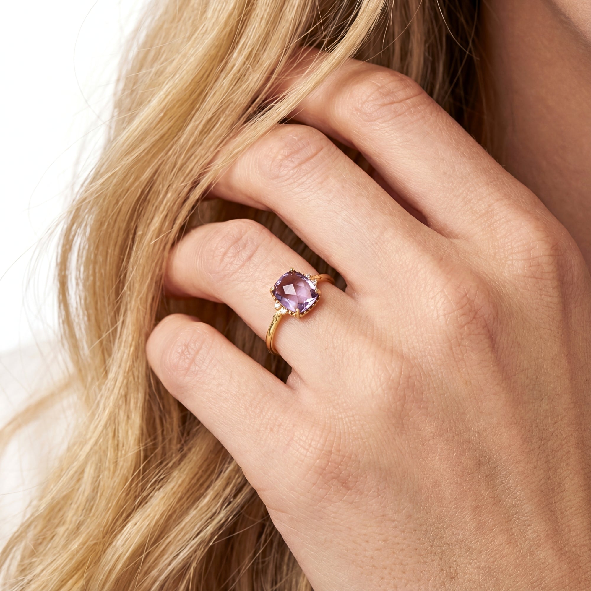 Close-up of a cushion cut simulated amethyst solitaire ring in 18K gold vermeil on a model's hand.