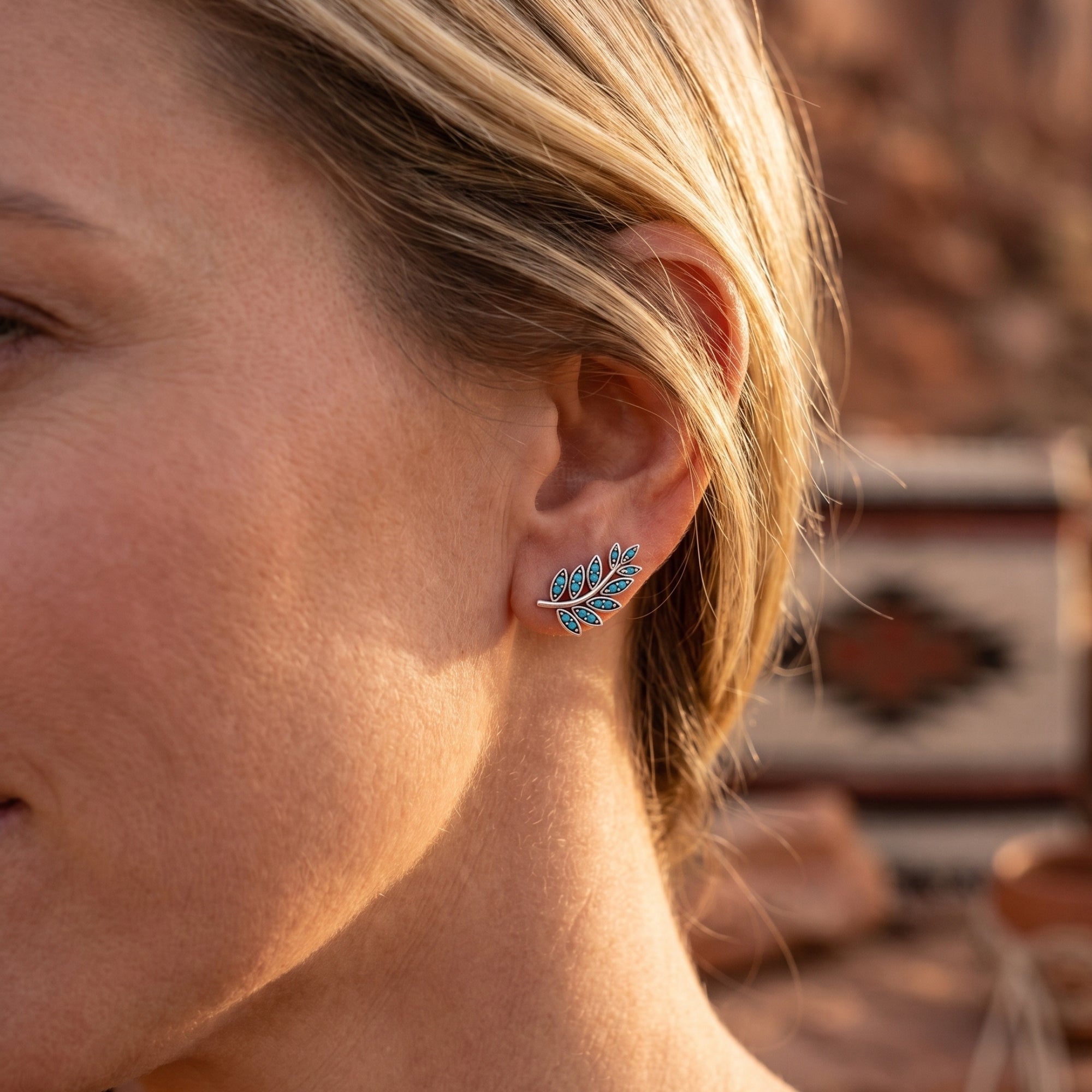 Woman wearing a silver Taos Turquoise leaf earring with round stones, shown against a desert landscape background.