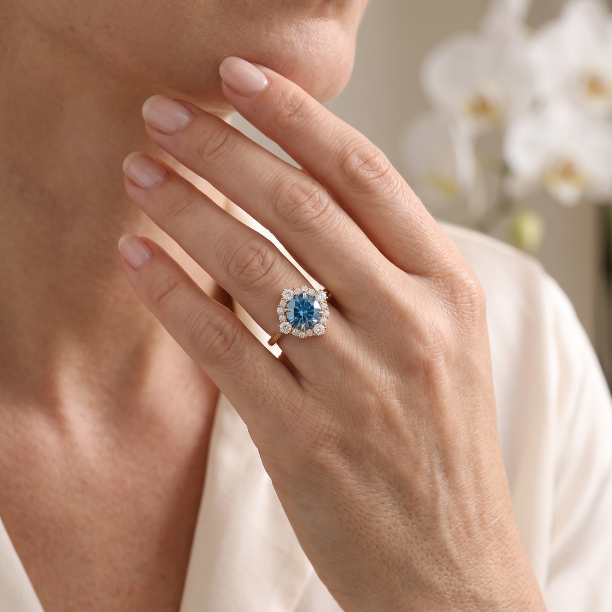 Lifestyle view of a round blue moissanite halo ring in rose gold worn on a woman's hand.