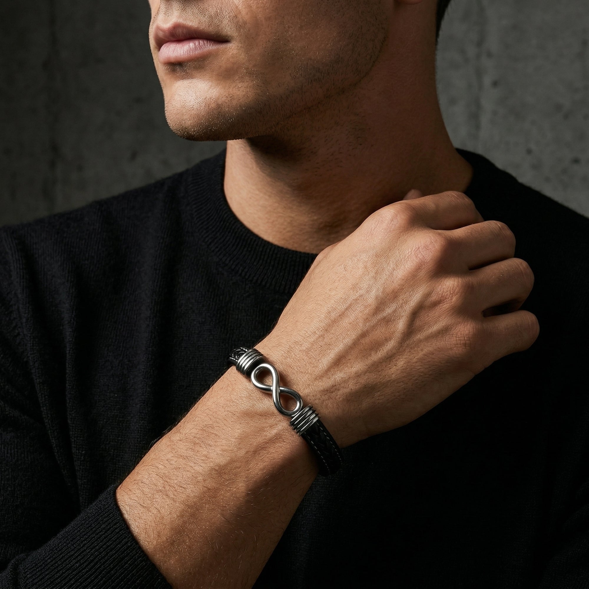 Men's black braided leather bracelet with a silver stainless steel infinity clasp, worn on a man's wrist.