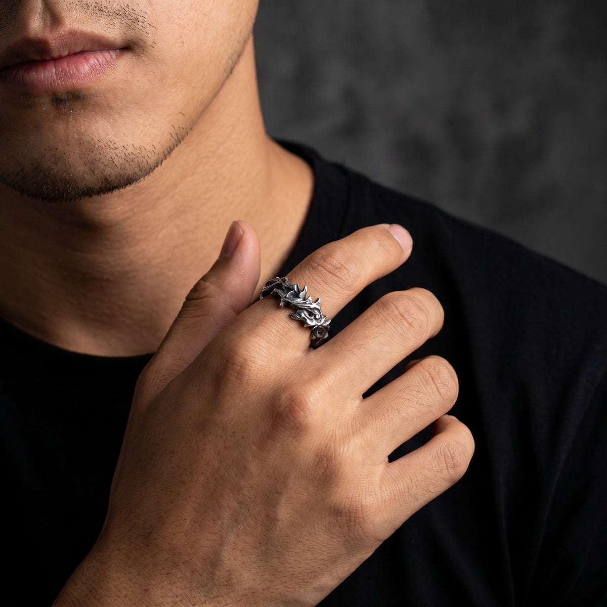 Model wearing the oxidized silver thorn open band ring on an index finger against a black shirt.