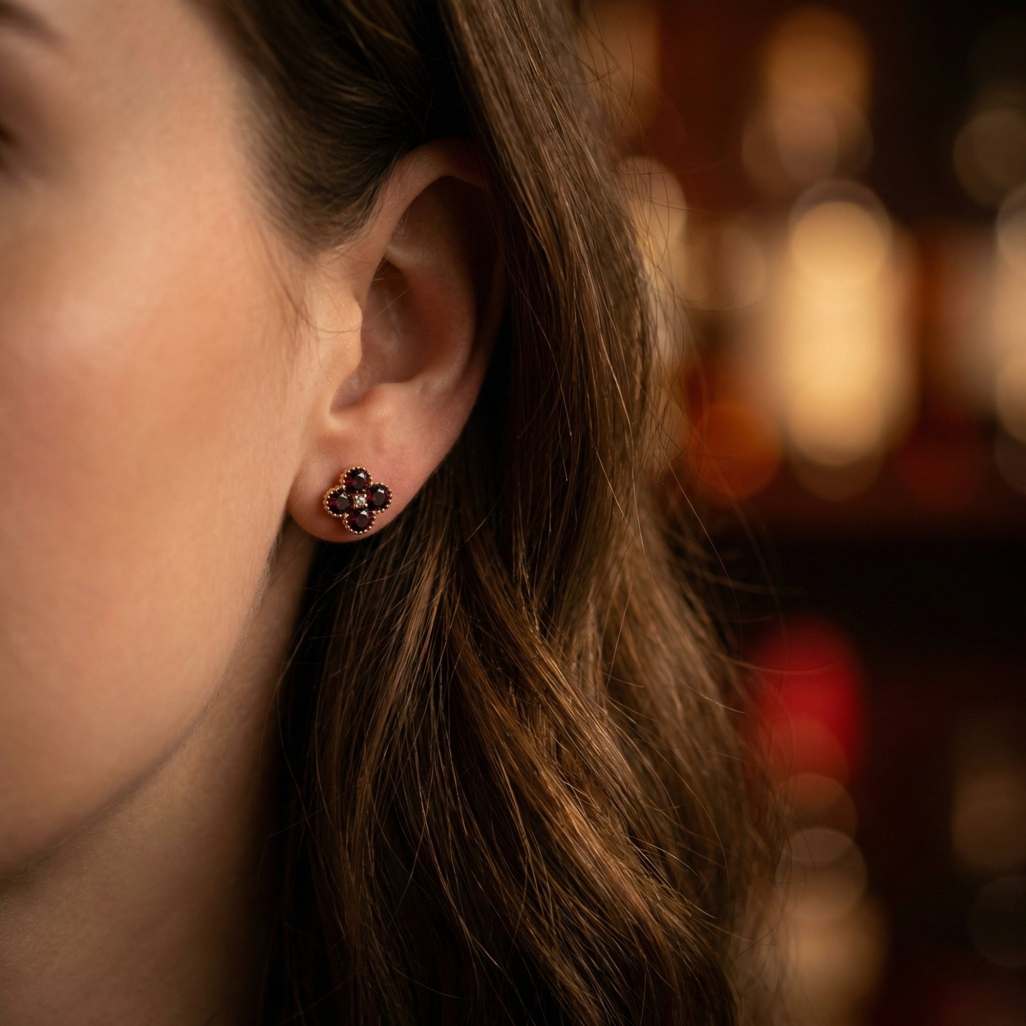 Woman wearing a yellow gold Ambrosia floral stud earring featuring round red garnets and a center diamond.