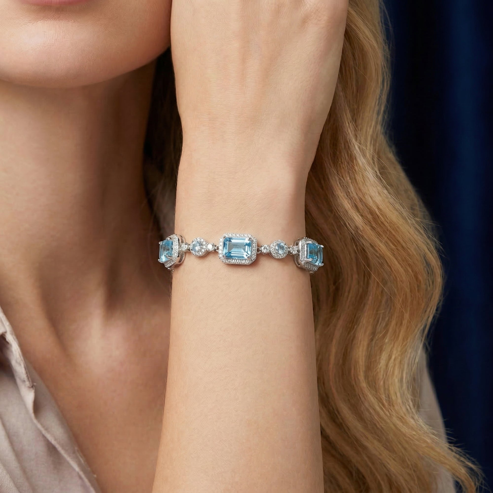Silver emerald cut blue topaz bracelet worn on a woman's wrist against a dark blue background.