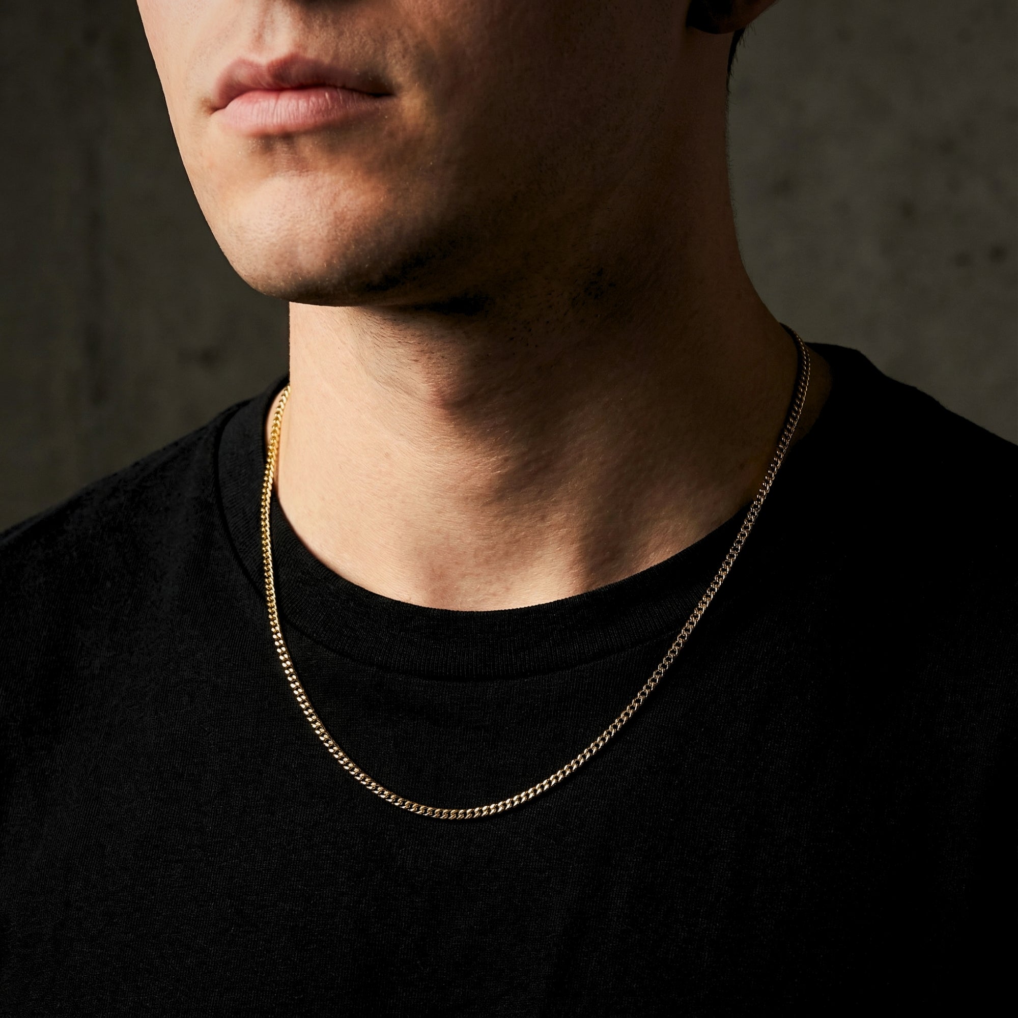 Model wearing the 2mm gold Connell stainless steel chain necklace over a black t-shirt.