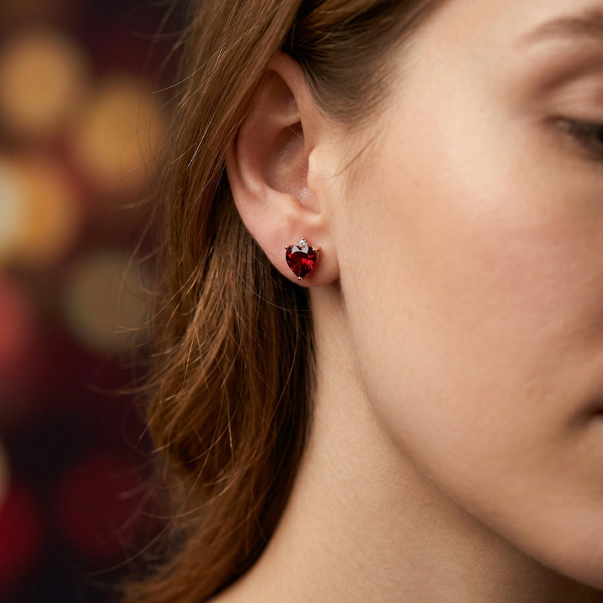 A woman wearing a heart-cut natural red garnet and 18K rose gold stud earring on her ear.
