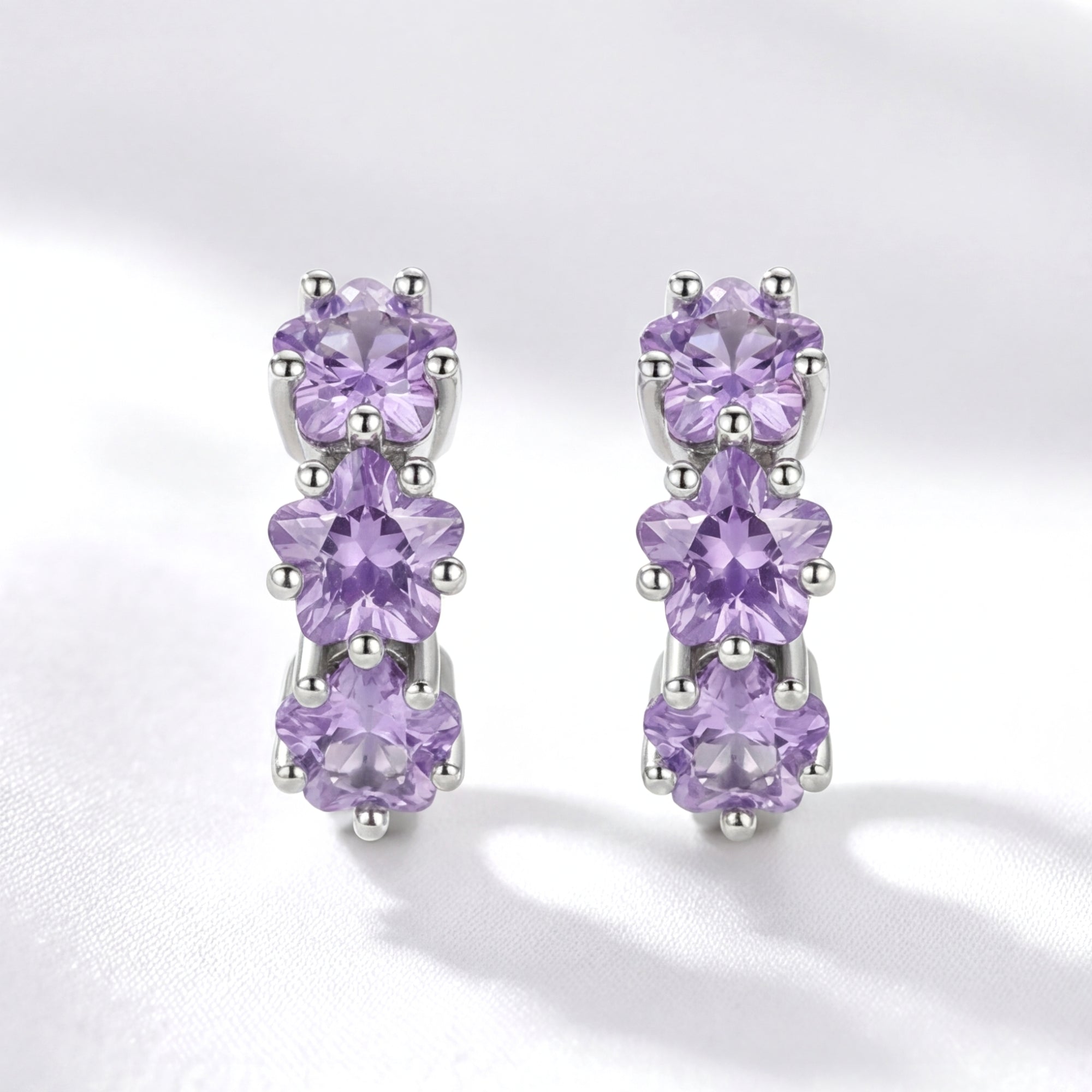 Front view of S925 sterling silver huggie earrings featuring triple star-cut purple simulated amethysts.
