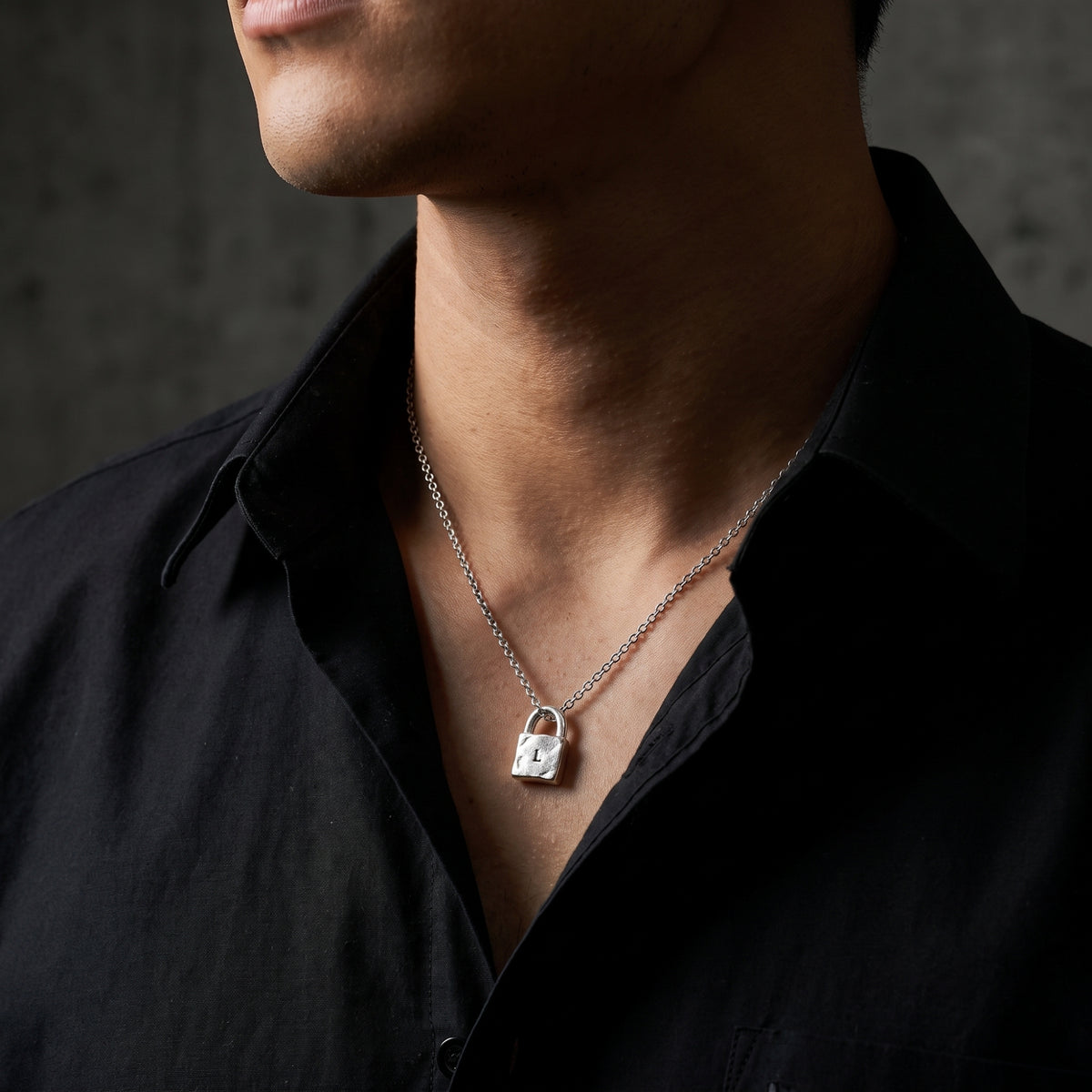 Close-up of a model wearing the silver stamped lock pendant necklace against an open black shirt collar.