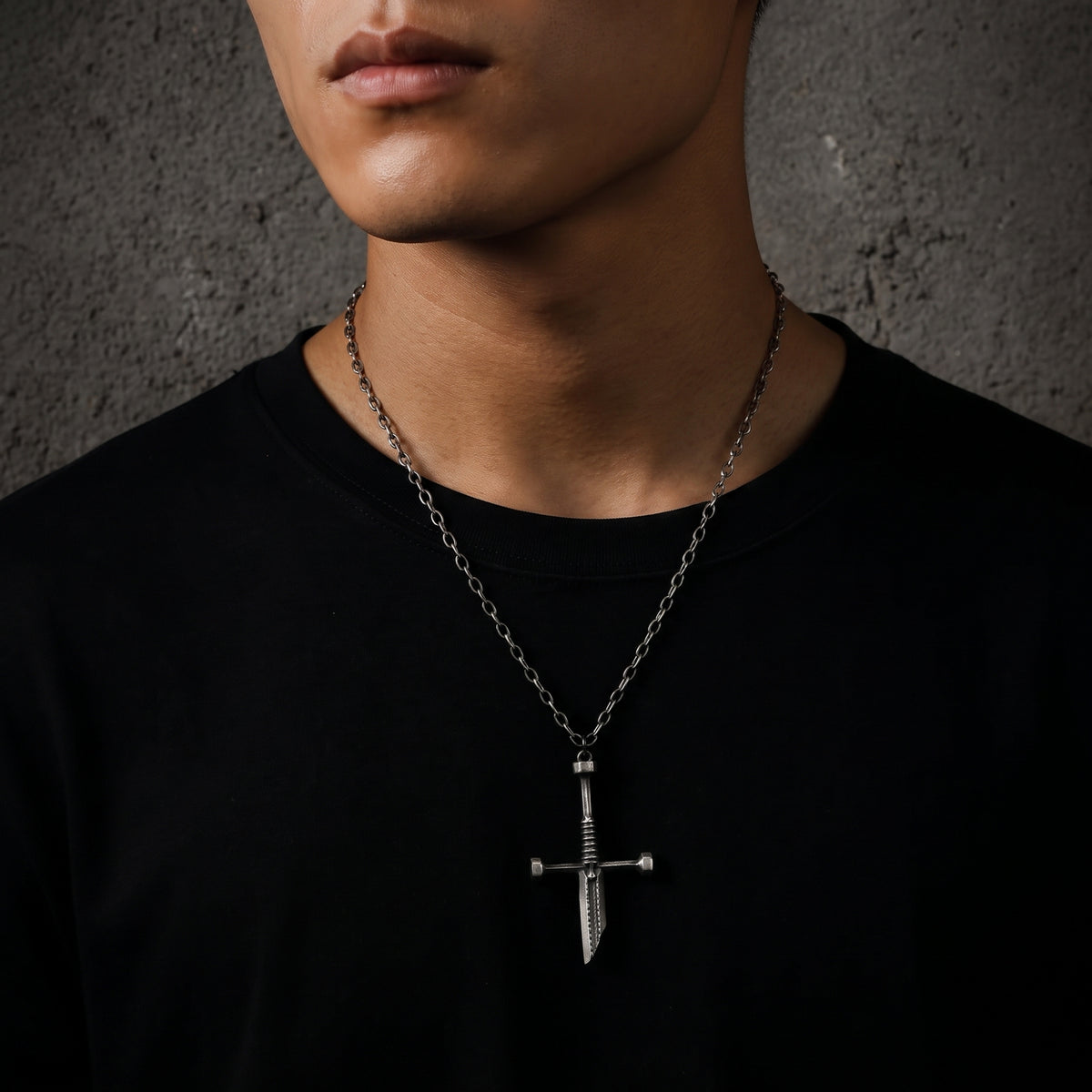 Male model wearing the silver dagger pendant on a chain over a plain black T-shirt.