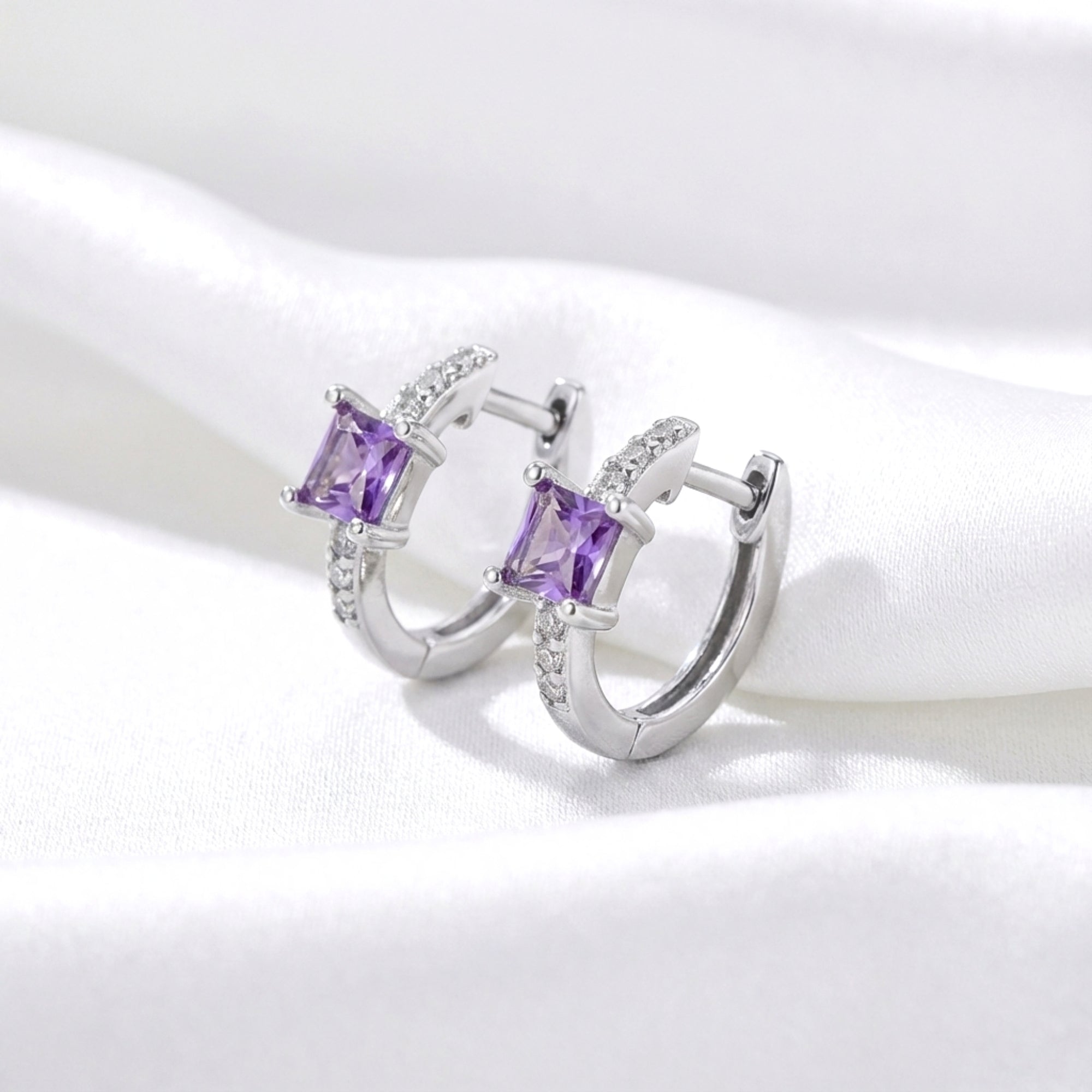 Side view of sterling silver huggie earrings featuring princess-cut purple simulated amethyst on white fabric.